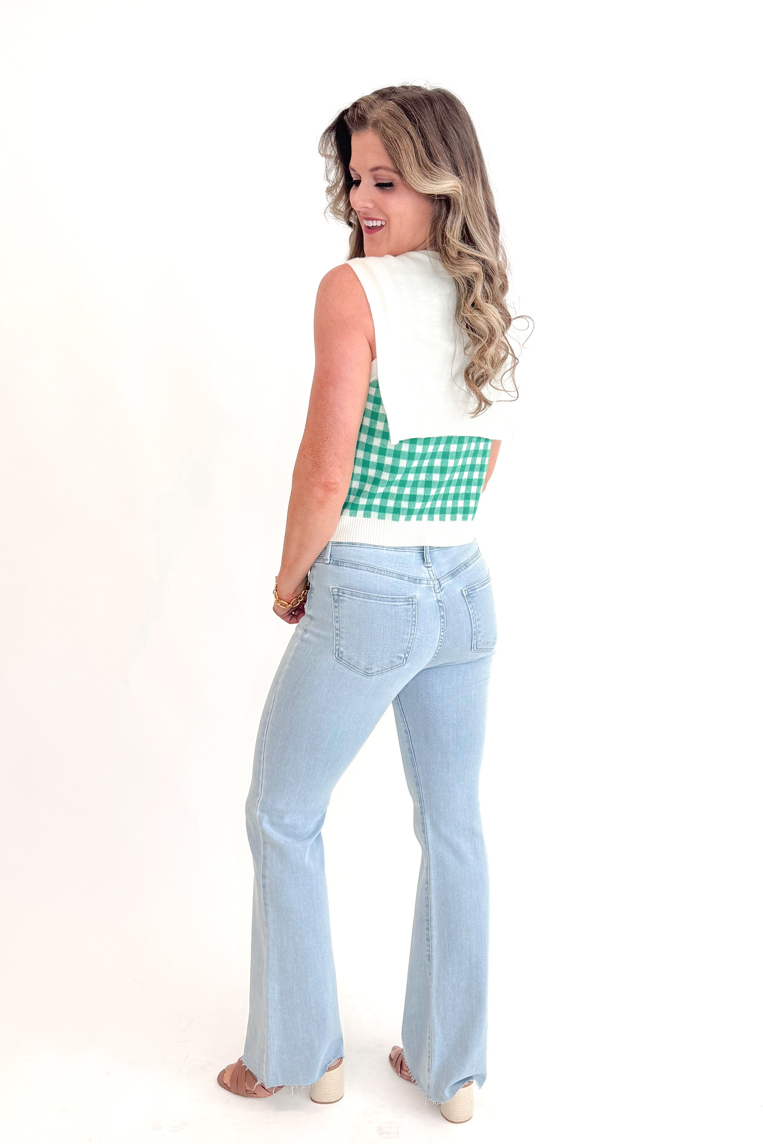 Side view of woman wearing Green Plaid Faux Layered Sweater Tank by Entro with jeans against white studio background.