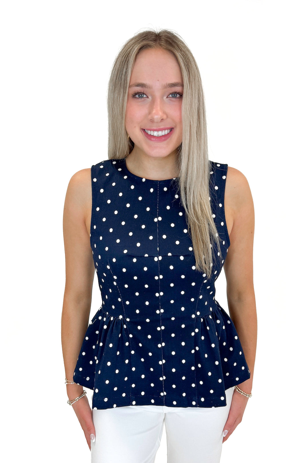 Front view of woman wearing Navy Polka Dot Peplum Tank by Entro with jeans against white studio background.