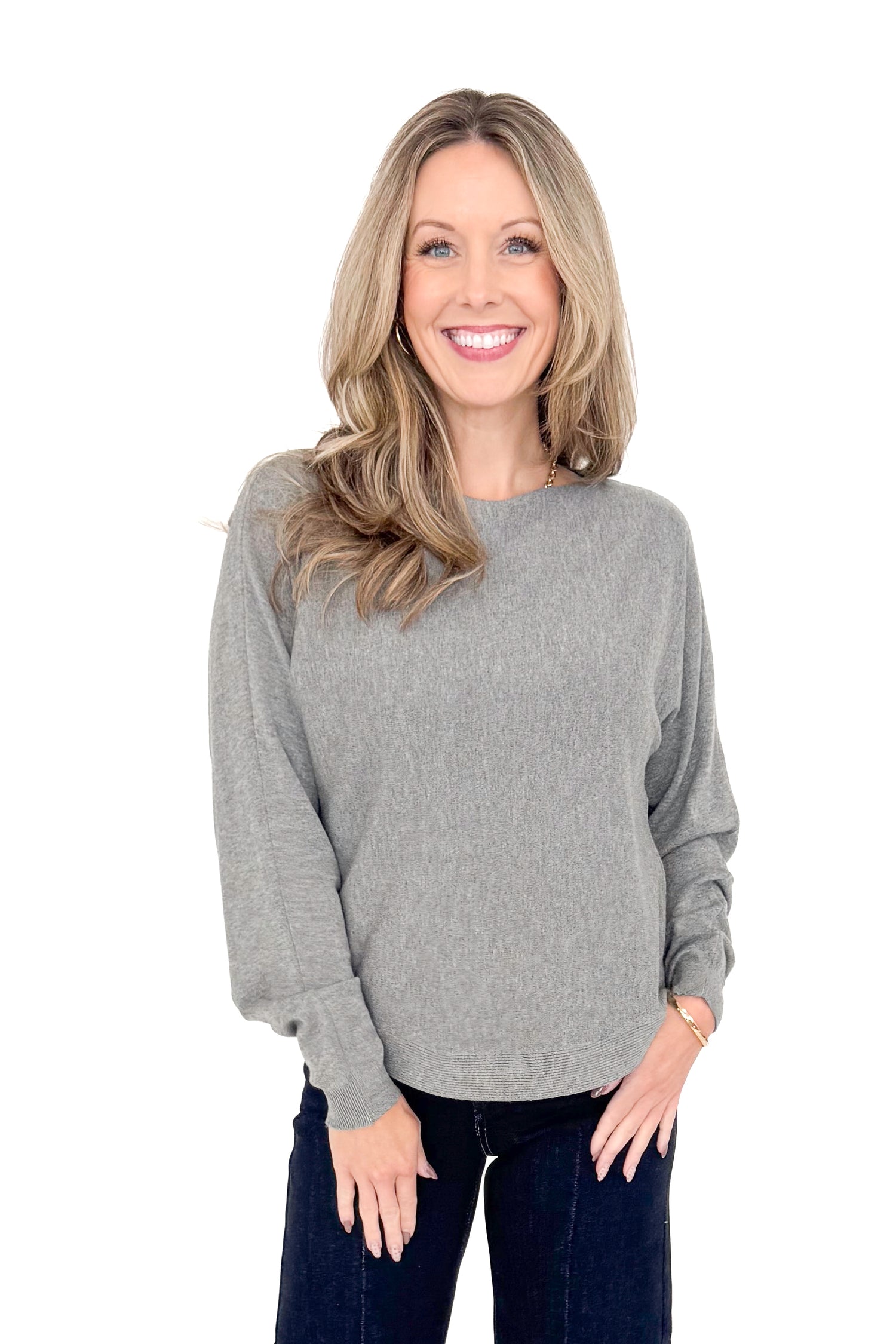 Front view of woman wearing grey sweater with jeans against white studio background.