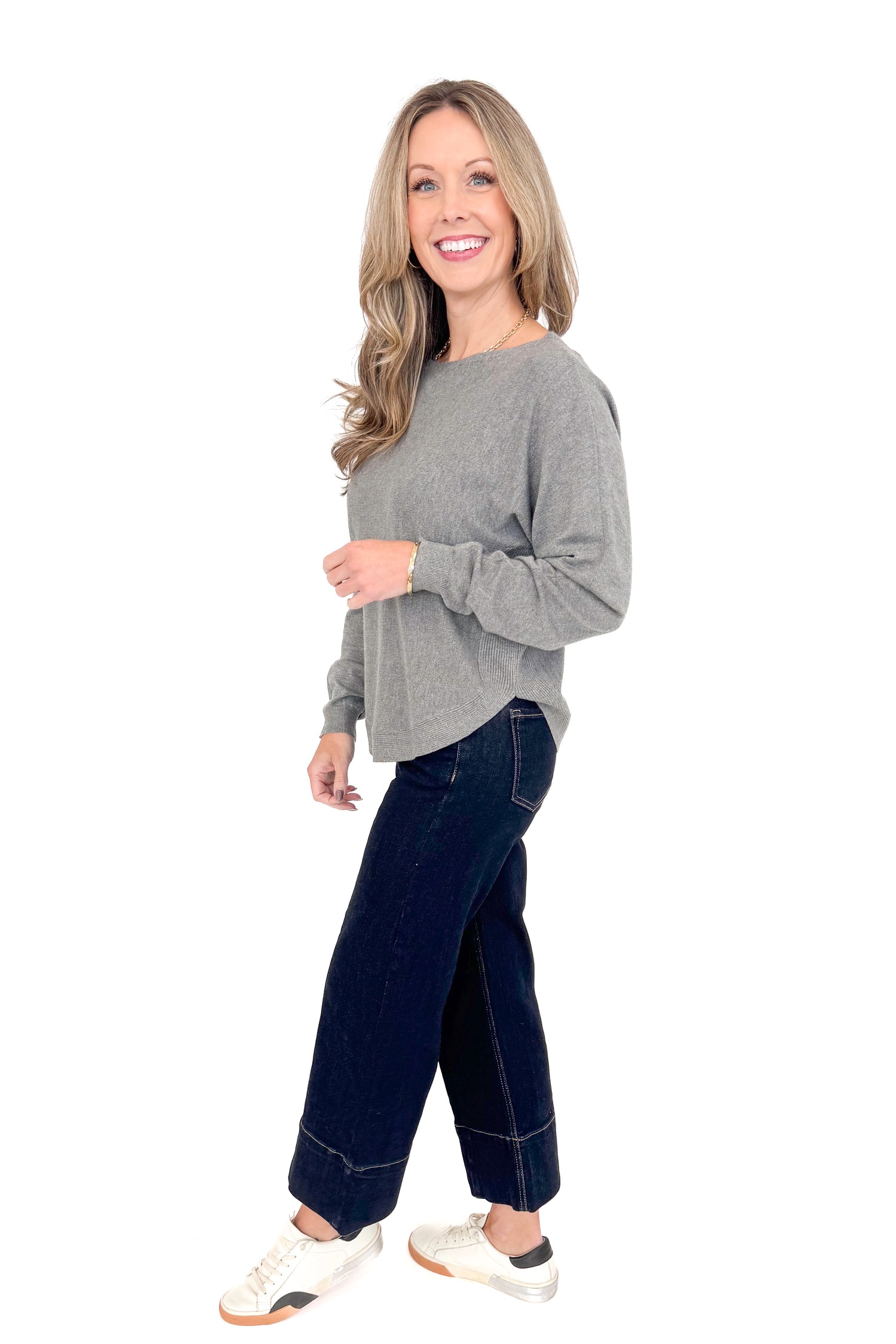 Side view of woman wearing grey sweater with jeans against white studio background.