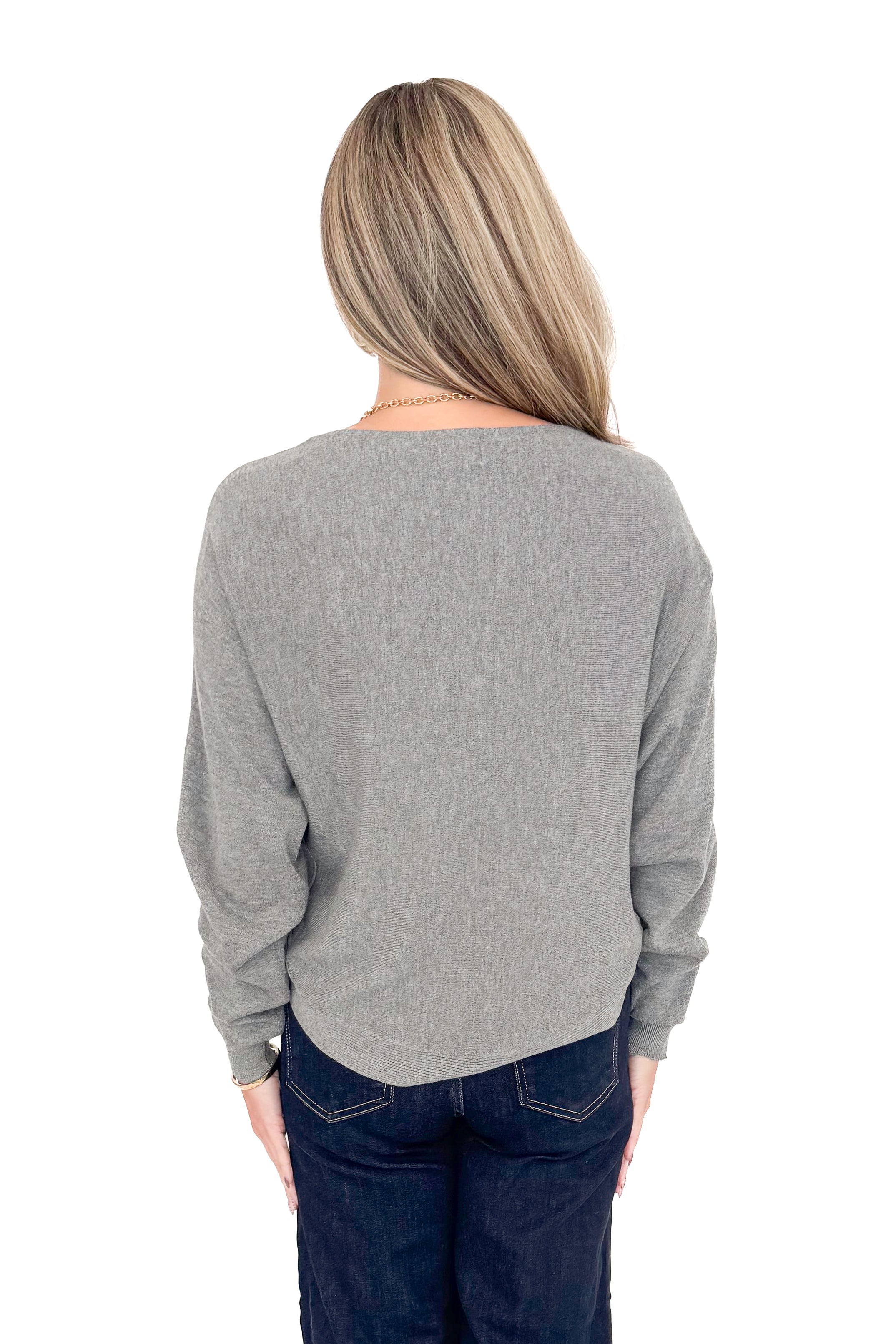 Back view of woman wearing grey sweater with jeans against white studio background.