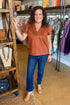 Woman in a store wearing a brown top and blue jeans, smiling.