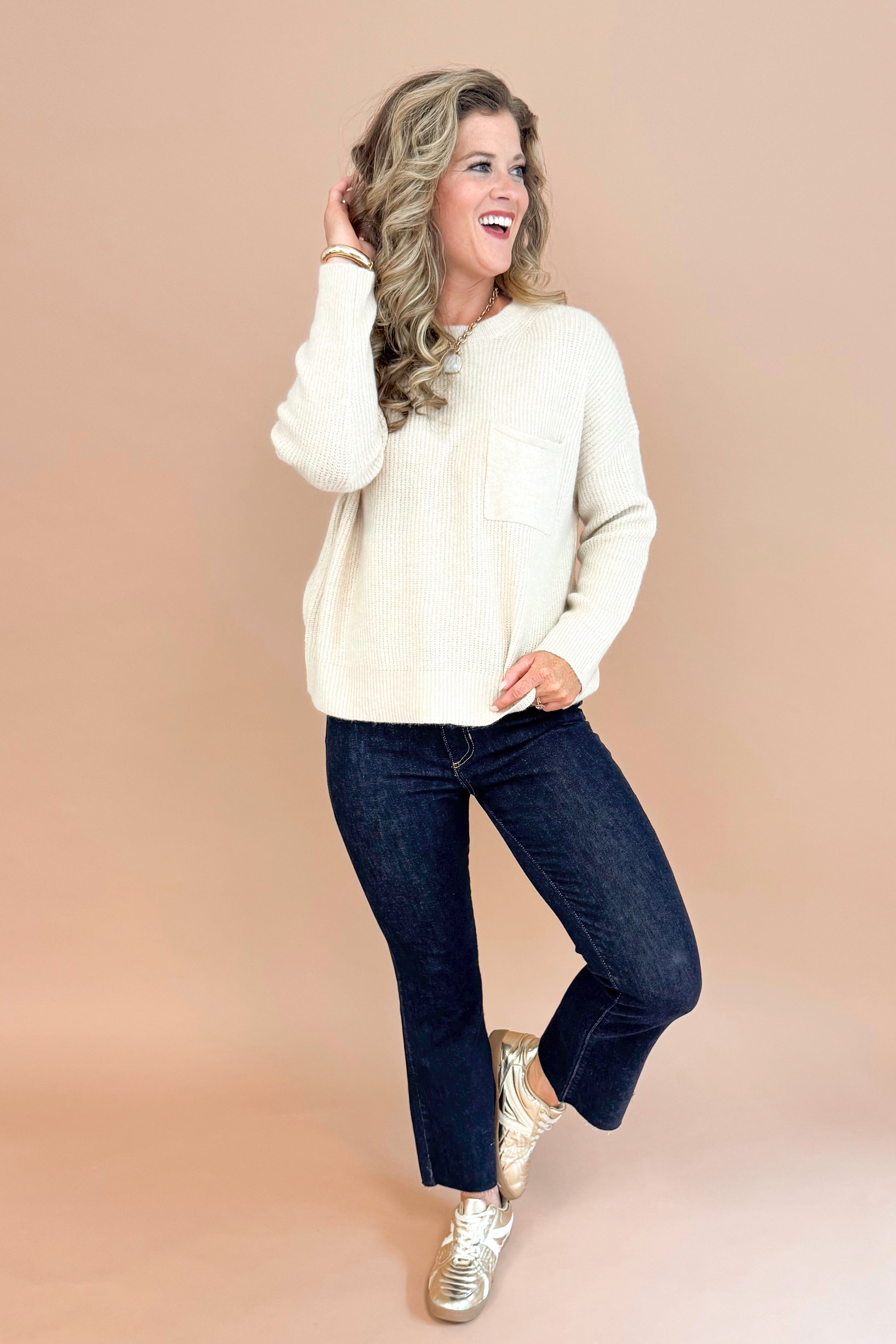 Woman wearing oatmeal colored crew neck pullover sweater with chest pocket detail and long sleeve full outfit.