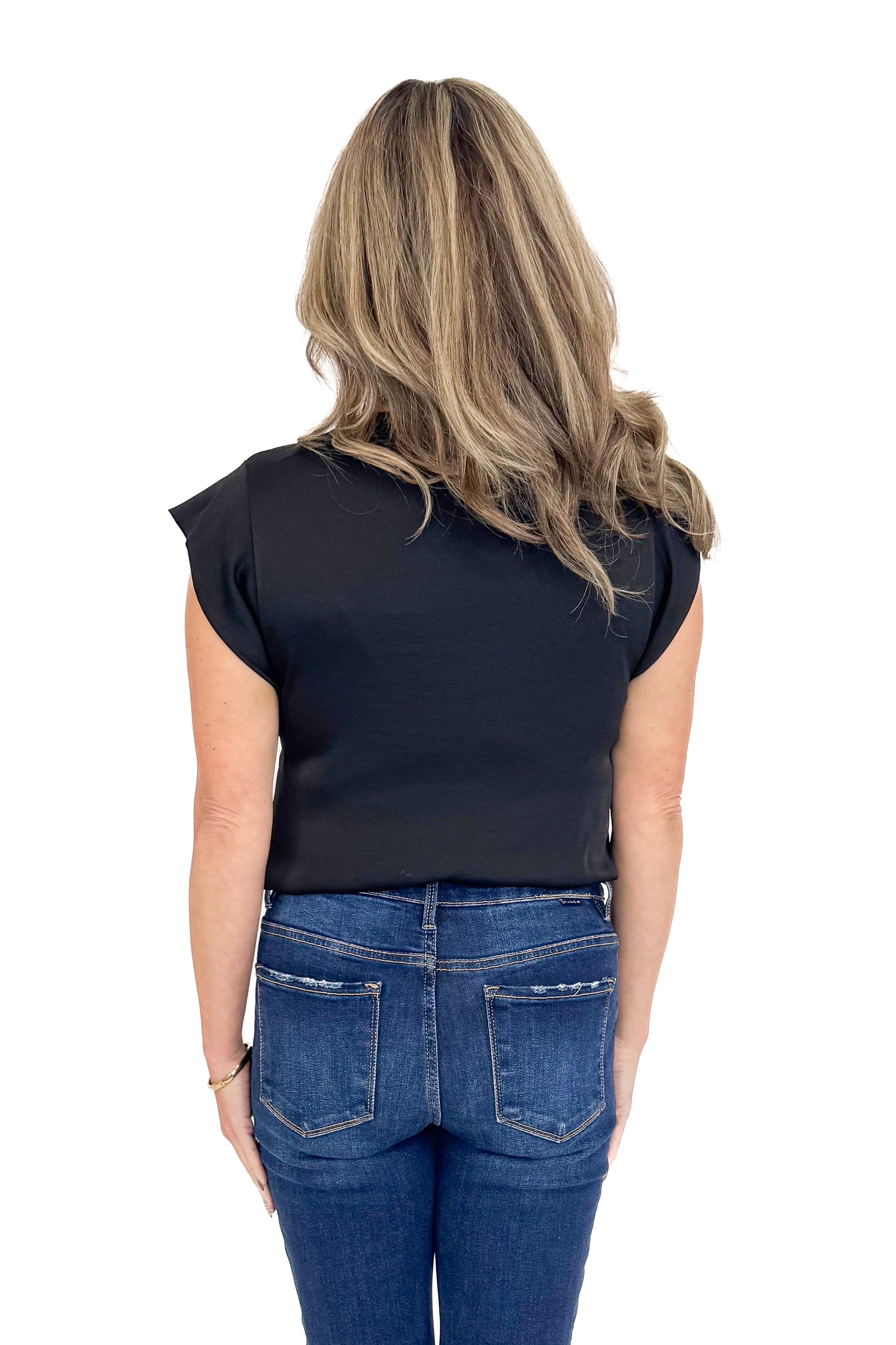 Back view of woman wearing black top with jeans against white studio background.