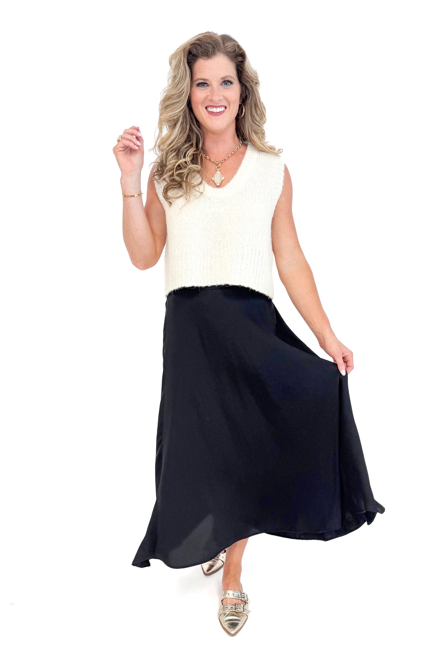 Front view of black satin swing skirt showing pleated detail and movement with cream sweater.