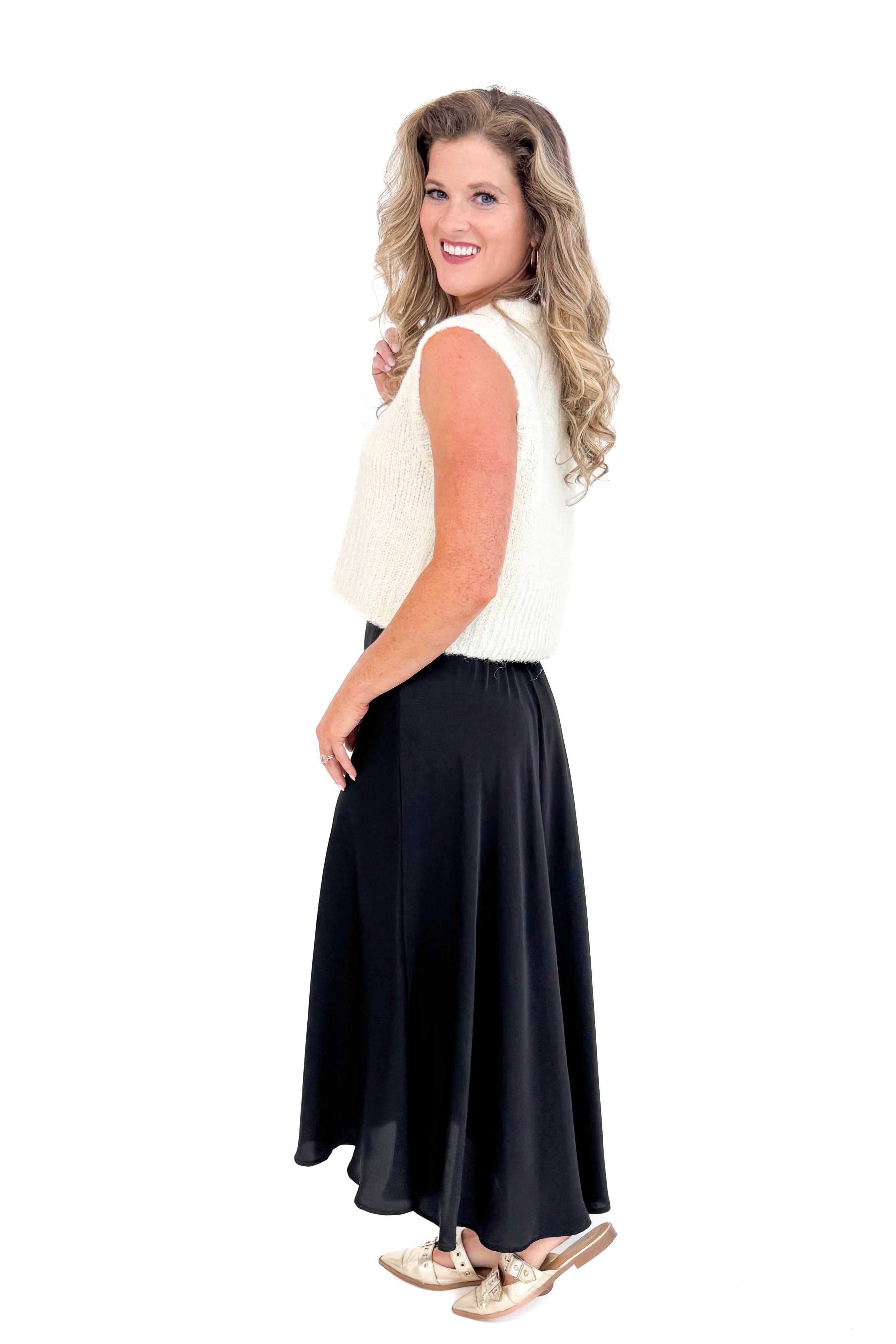 Side view of black satin swing skirt showing pleated detail and cream sweater.