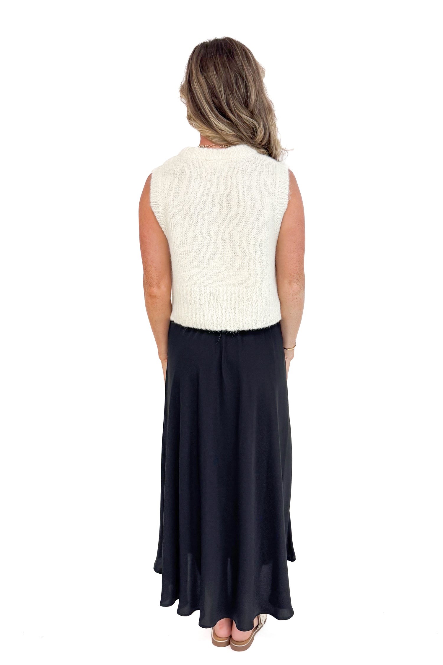 Back view of woman modeling black satin swing skirt showing pleated detail.