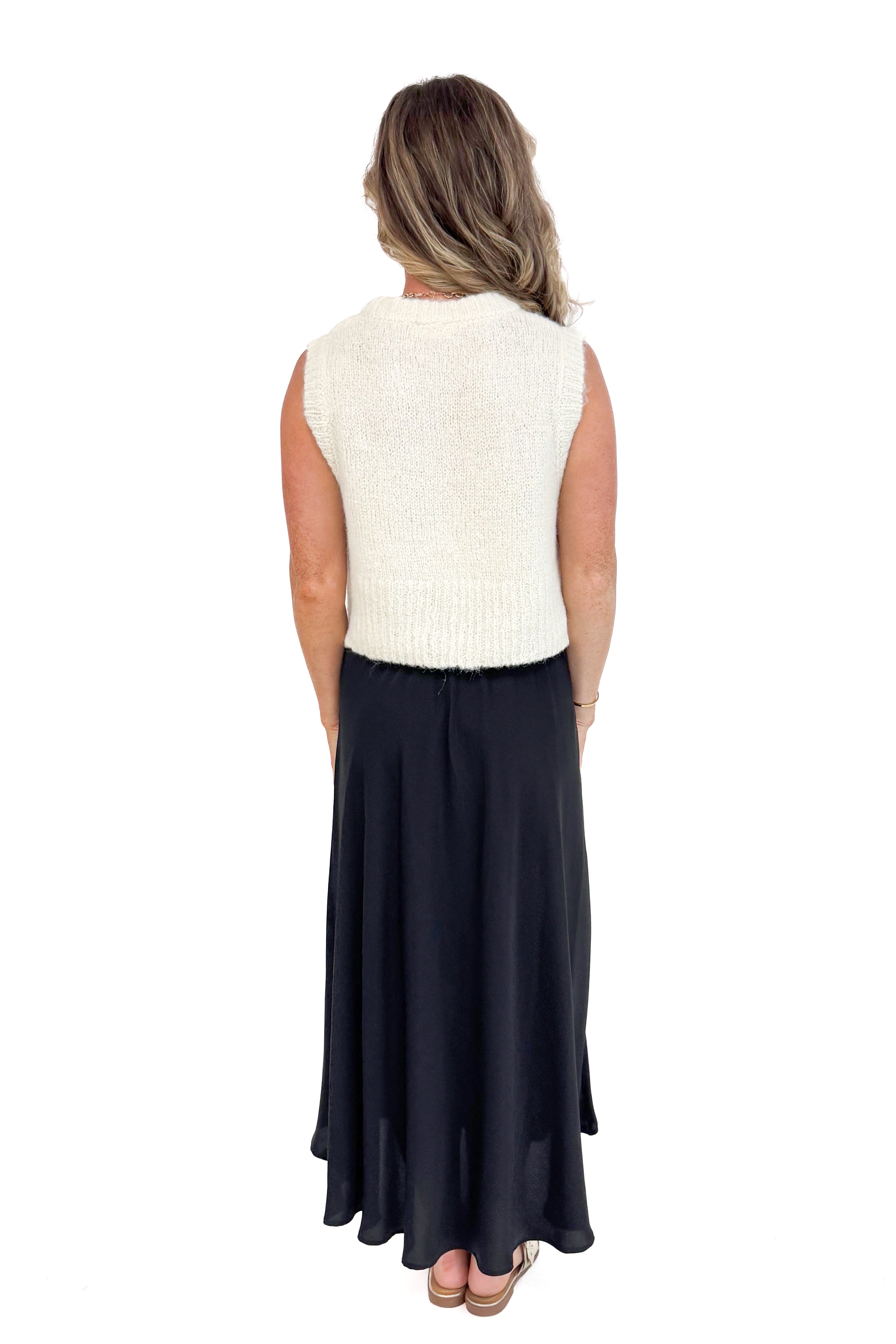 Back view of woman modeling black satin swing skirt showing pleated detail.