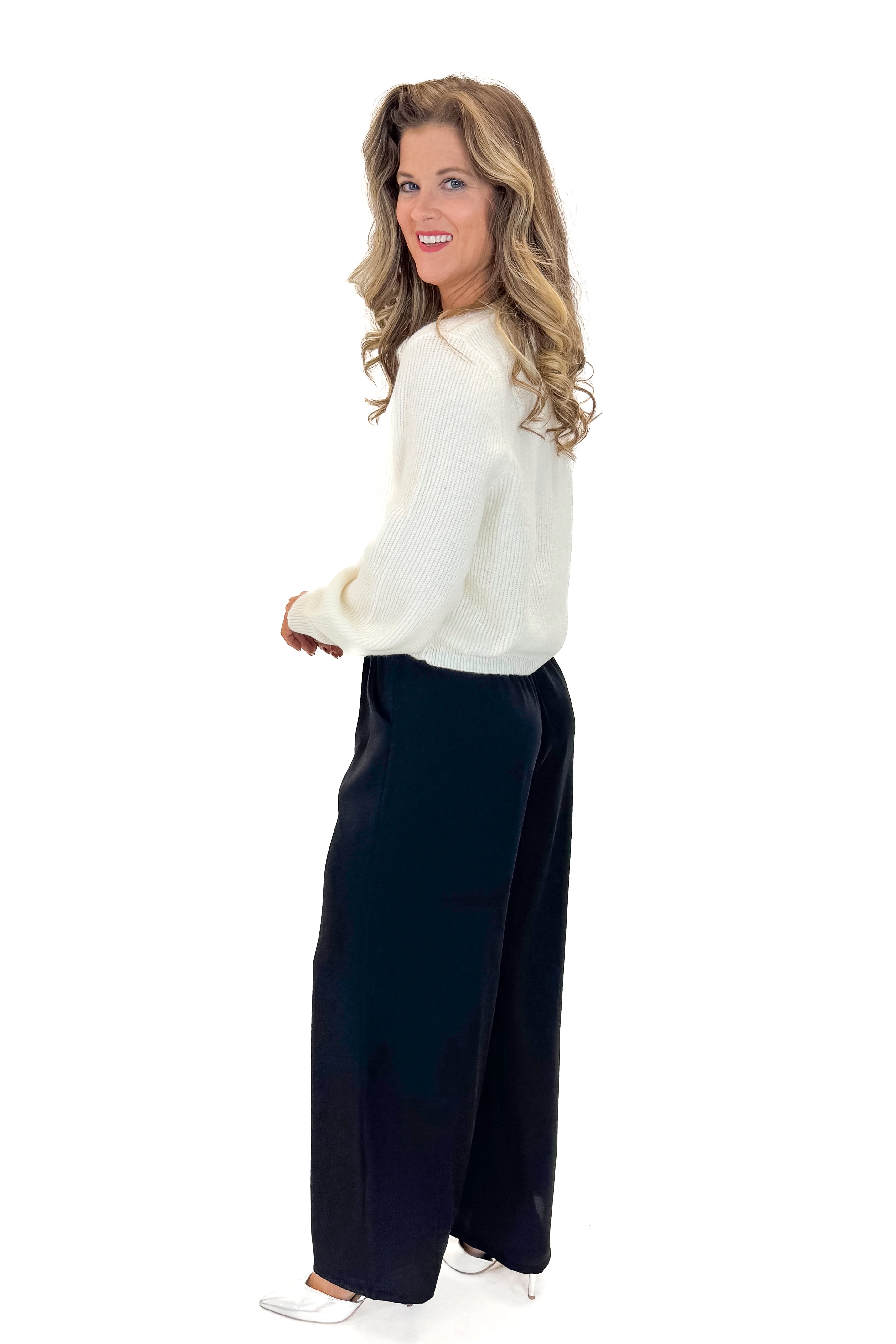 Side view of woman wearing sweater with Black Satin Pants against white studio background.