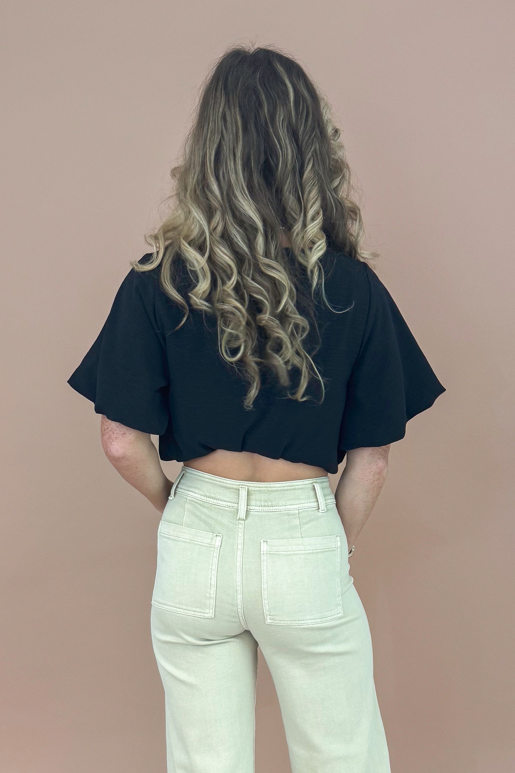 Person wearing a black crop top and white pants against a beige background