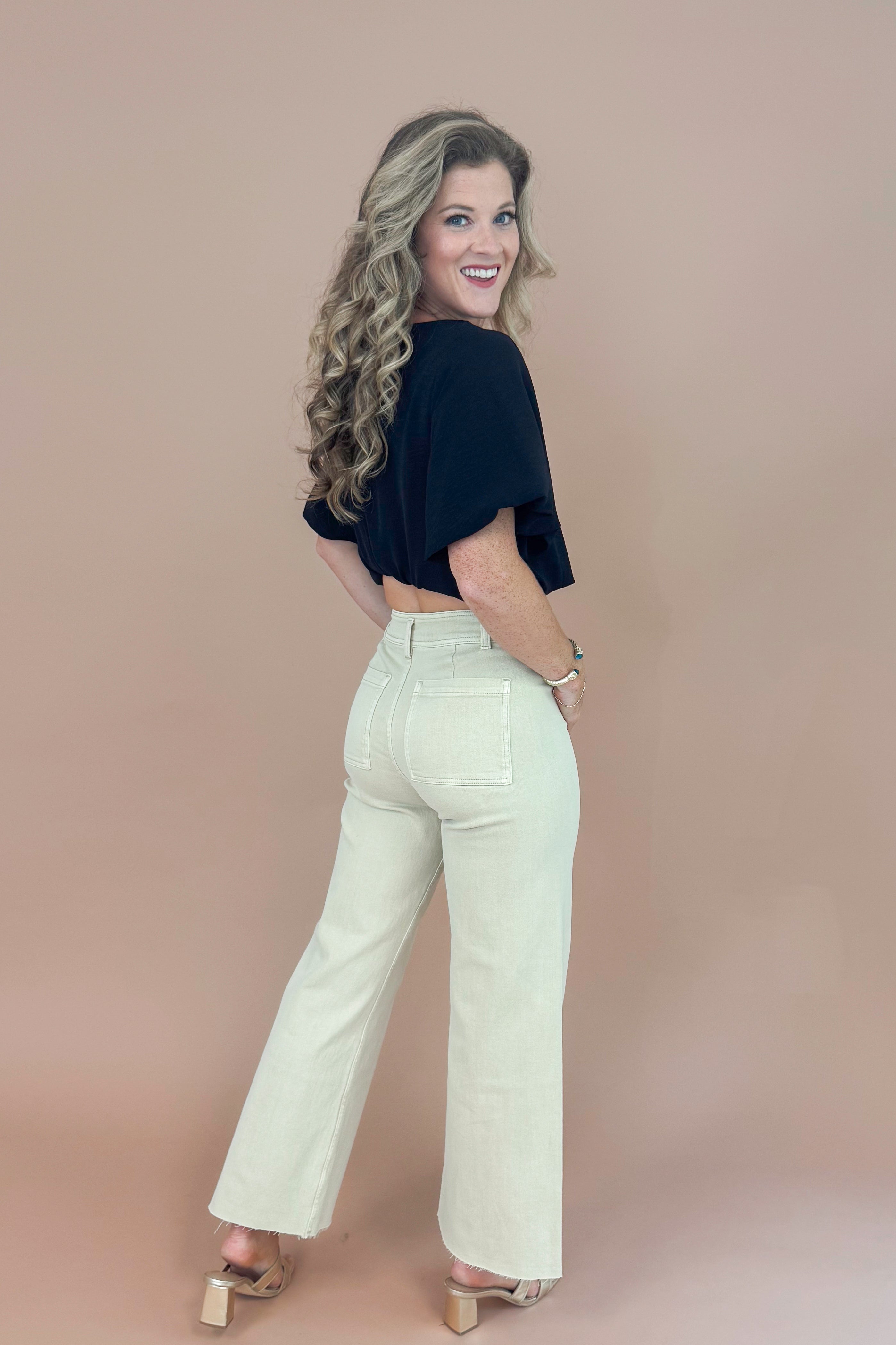 Woman wearing a black top and light-colored pants against a beige background