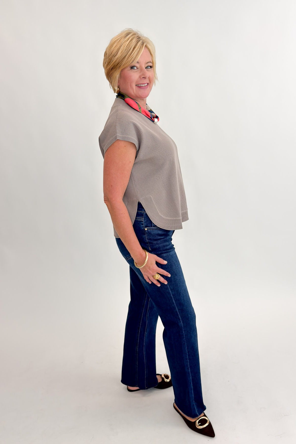 Side view of woman wearing Swagger Boutique’s Taupe Ribbed Short Sleeve Sweater by Entro with jeans against white studio background.