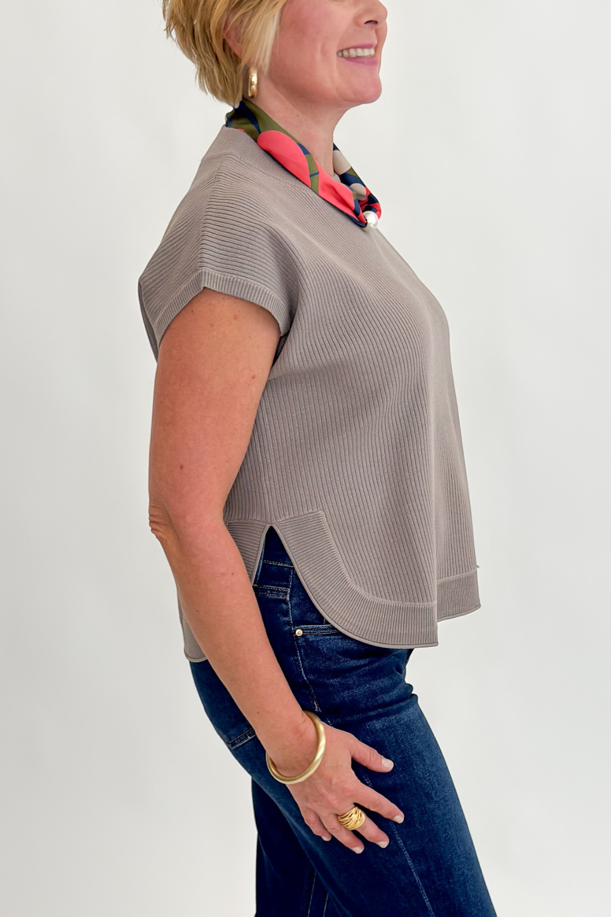 Side detail view of woman wearing Swagger Boutique’s Taupe Ribbed Short Sleeve Sweater by Entro with jeans against white studio background.