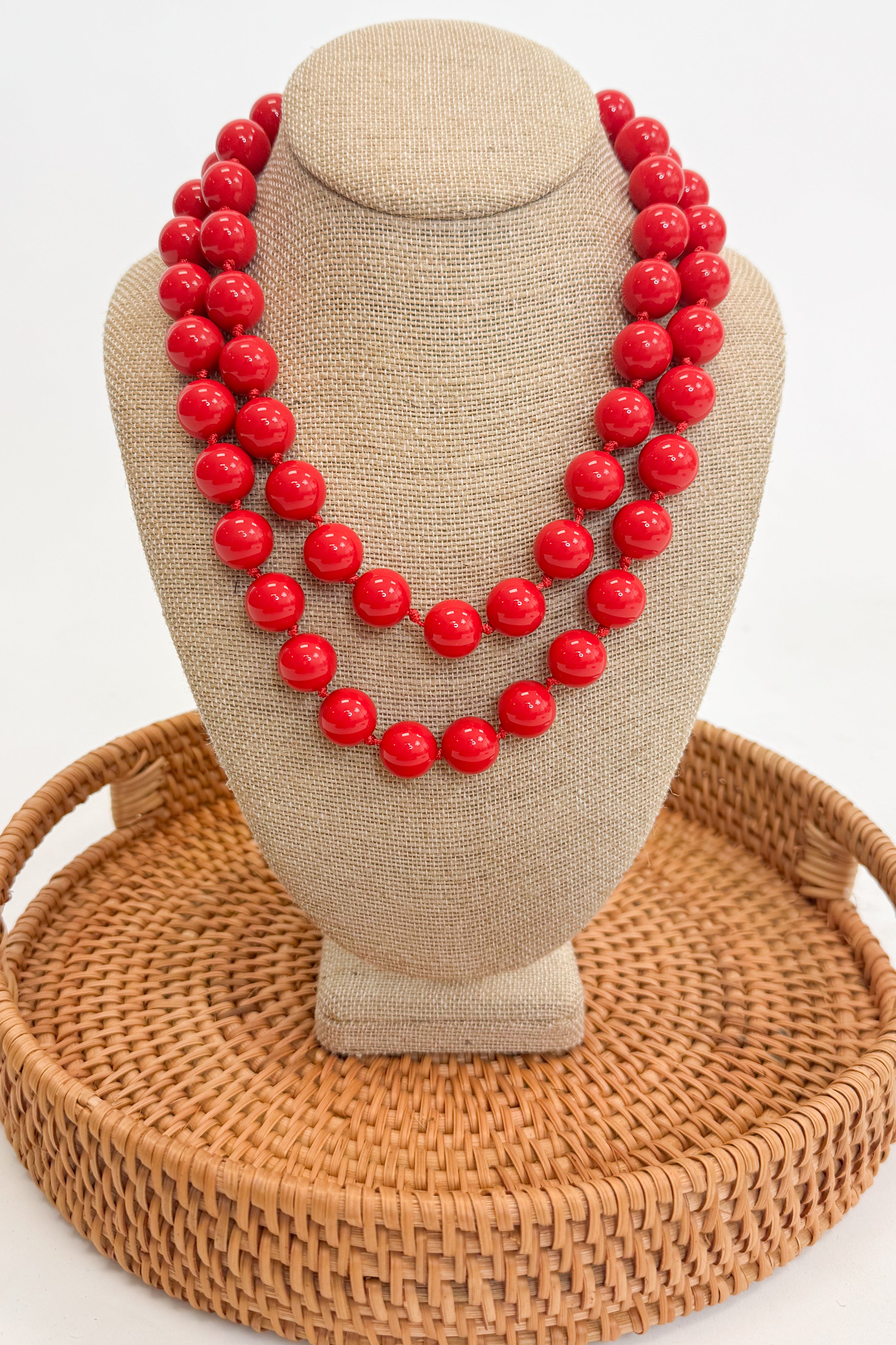 Red beaded necklace on a beige mannequin bust with a woven brown base.