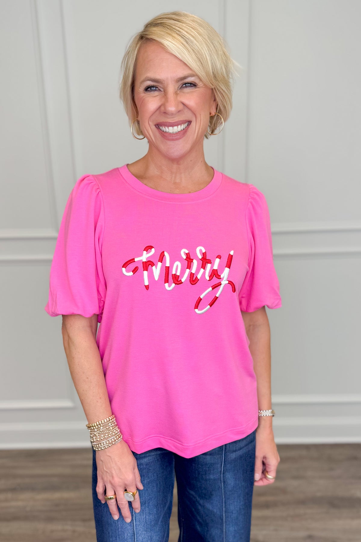 A smiling blonde woman wearing a bright pink short-sleeve t-shirt with &