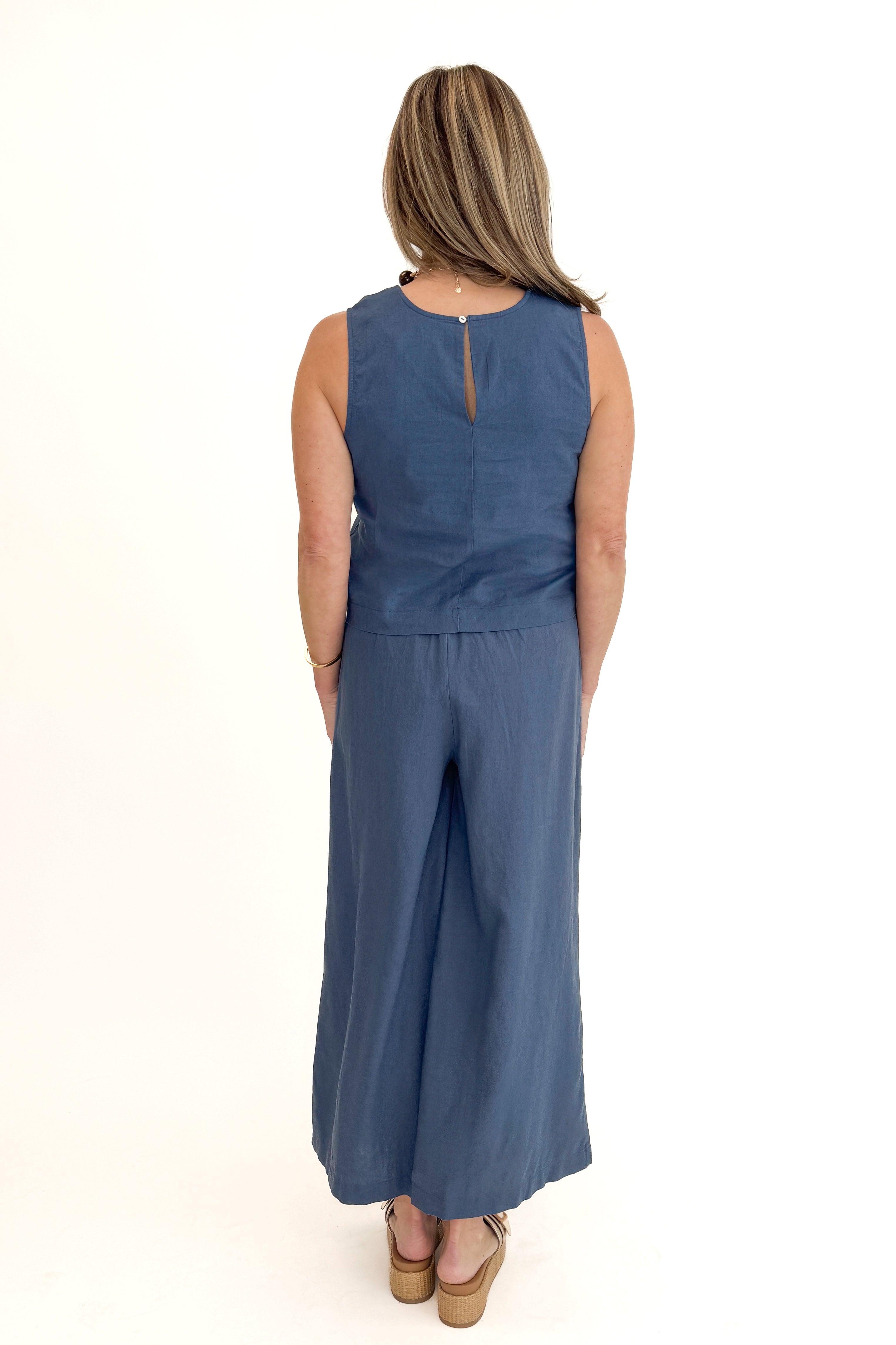 Back view of woman wearing Vintage Indigo Scout Linen Pants by Z Supply with matching Vintage Indigo Sloane Linen Top by Z Supply against white studio background.