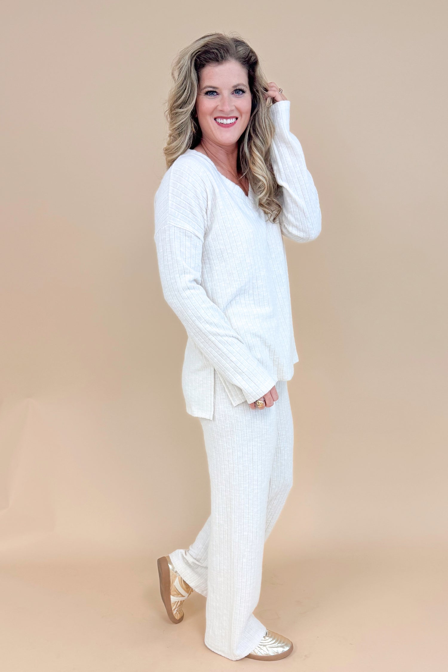 Side view of model wearing cream ribbed lounge pants and matching long sleeve top.