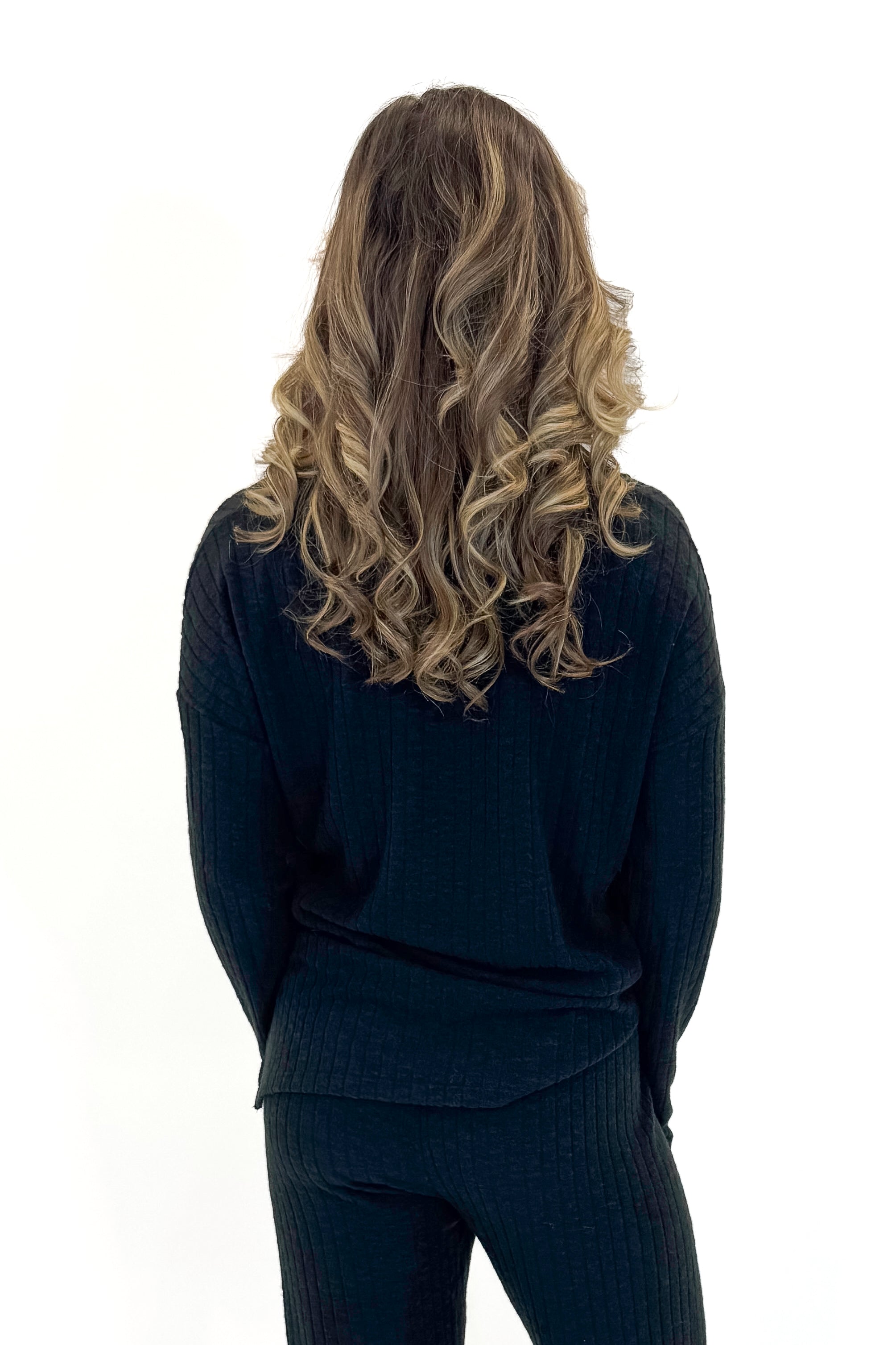 Back view of woman wearing Black Ribbed V-neck Long Sleeve Top with matching pants against white studio background.