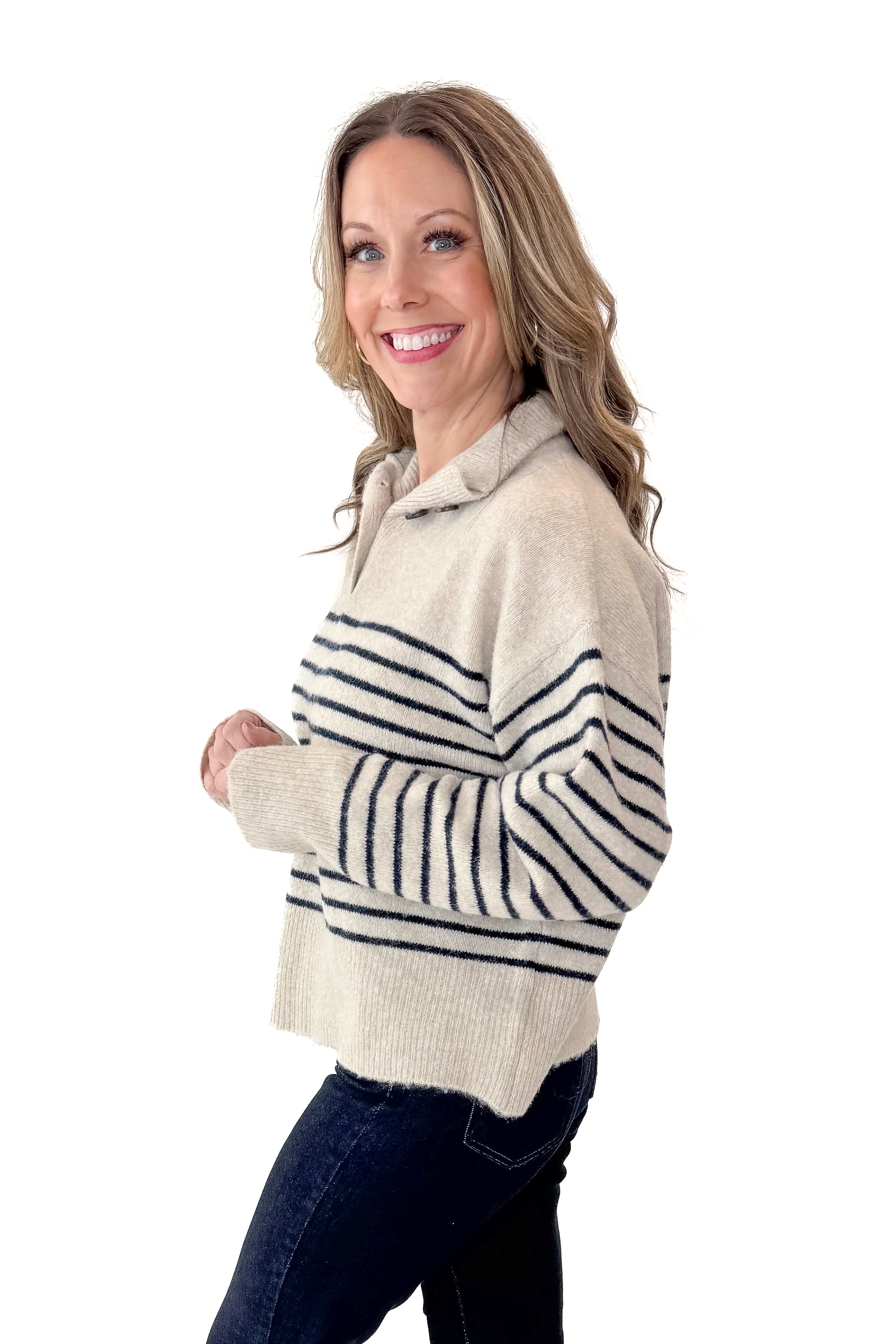 Side view of woman wearing Oatmeal and Navy Striped Button Detail Sweater with jeans against white studio background.