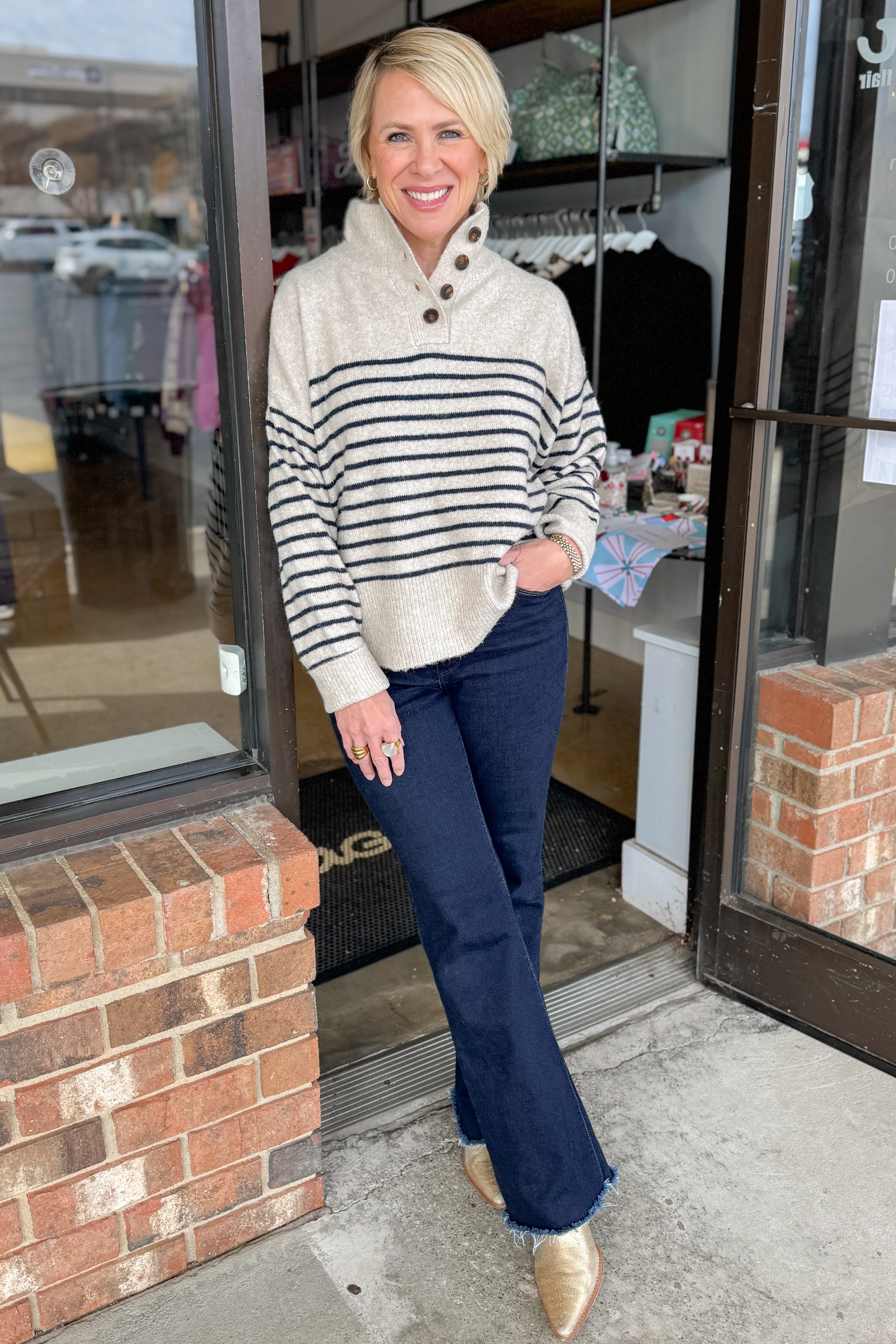 Front view of woman wearing Oatmeal and Navy Striped Button Detail Sweater with jeans at a boutique.