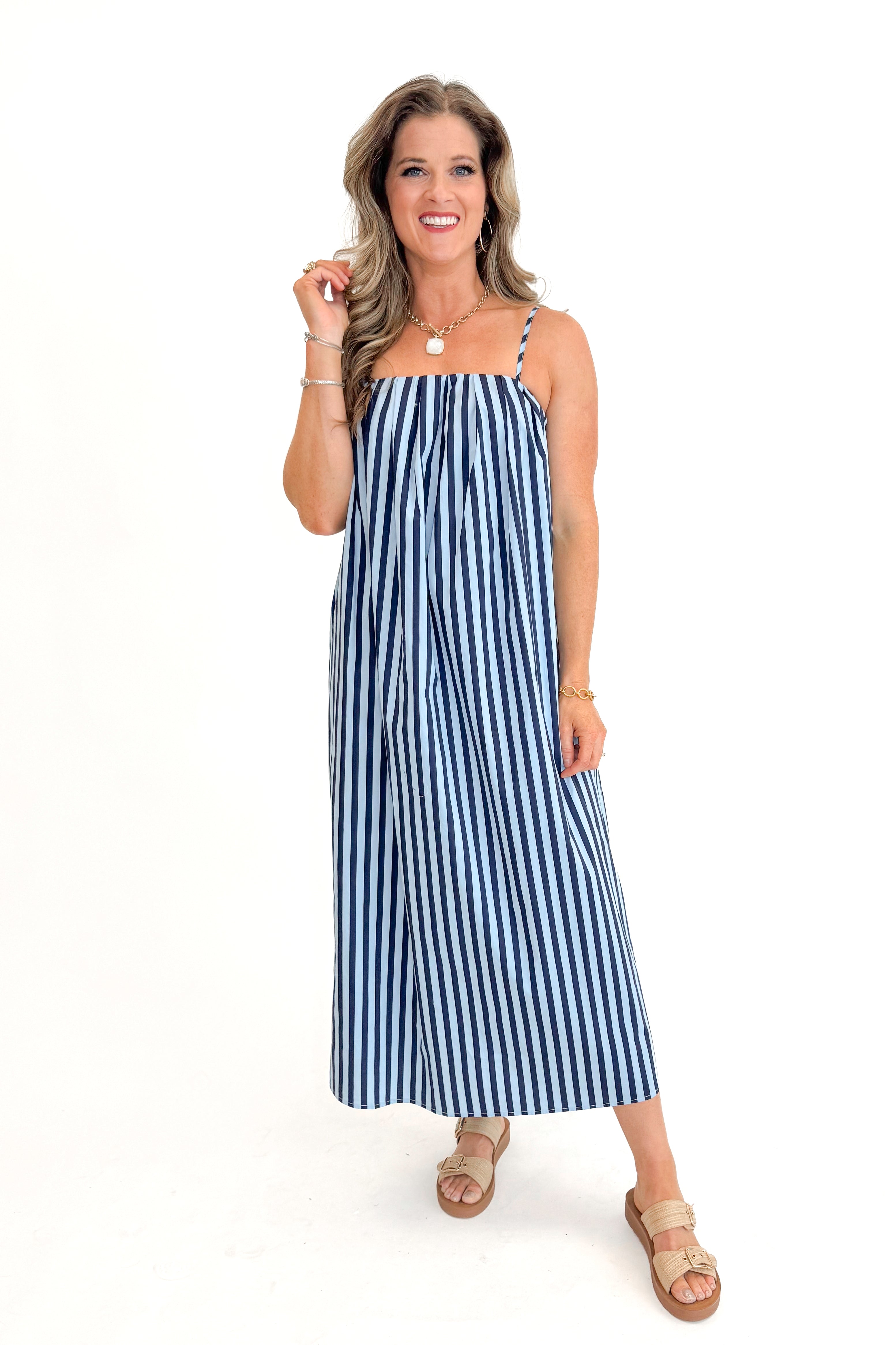 Front view of woman wearing Blue & Navy Striped Midi Dress with sandals against white studio background.