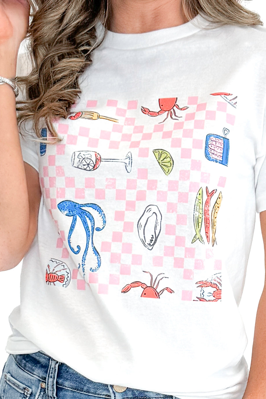 Front detail view of woman wearing Fish & Checkered Graphic Tee with jeans against white studio background.