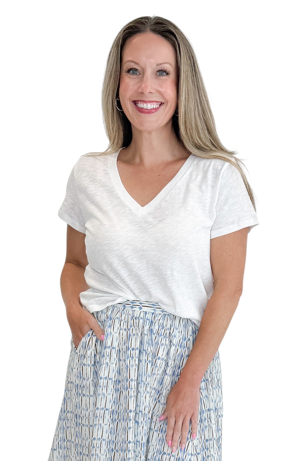 Front view of woman wearing Swagger Boutiqueās White Nomad V-Neck Tee by Z Supply with skirt against white studio background.
