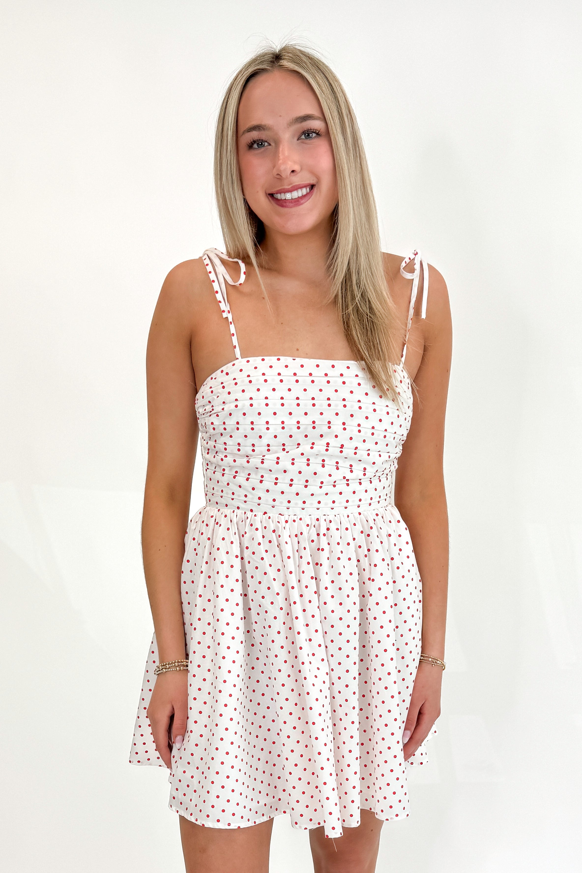 Front view of woman wearing Swagger Boutique’s White With Red Polka Dots Tie Strap Dress with sandals against white studio background.