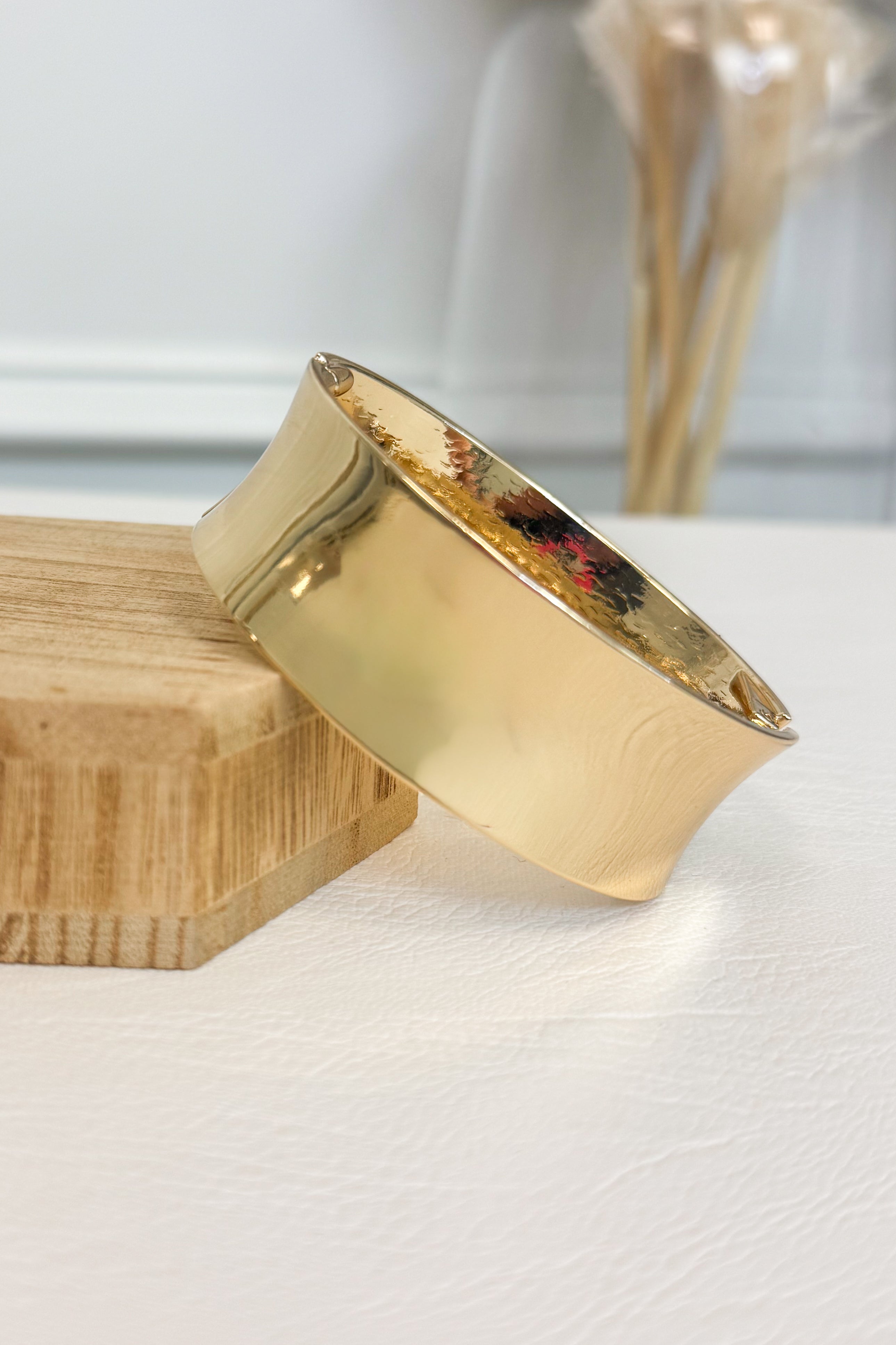 Gold-tone wide bracelet featuring a smooth rounded band on a white studio background