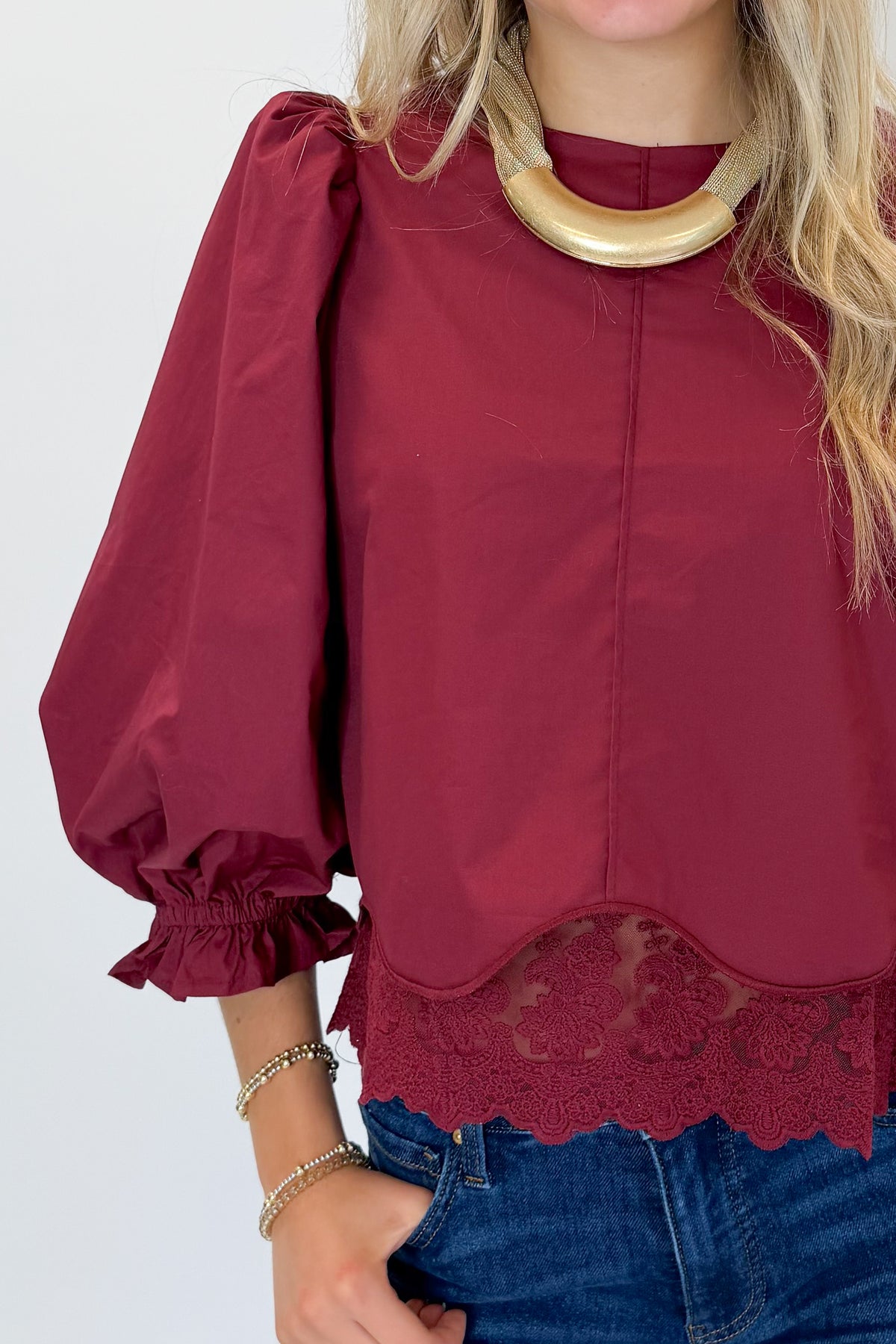 Front detail view of woman wearing Swagger Boutique’s Wine Lace Trim Top by Entro with jeans against white studio background.