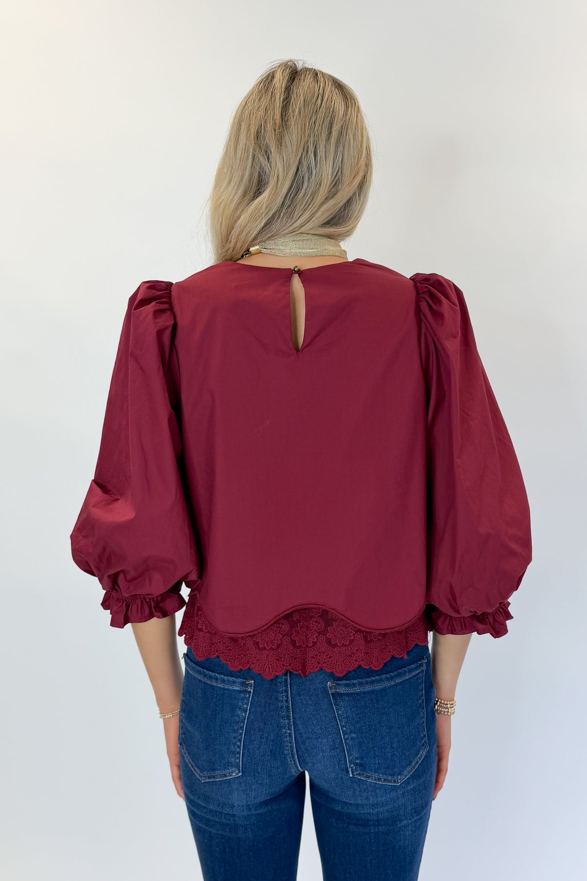Back view of woman wearing Swagger Boutique’s Wine Lace Trim Top by Entro with jeans against white studio background.