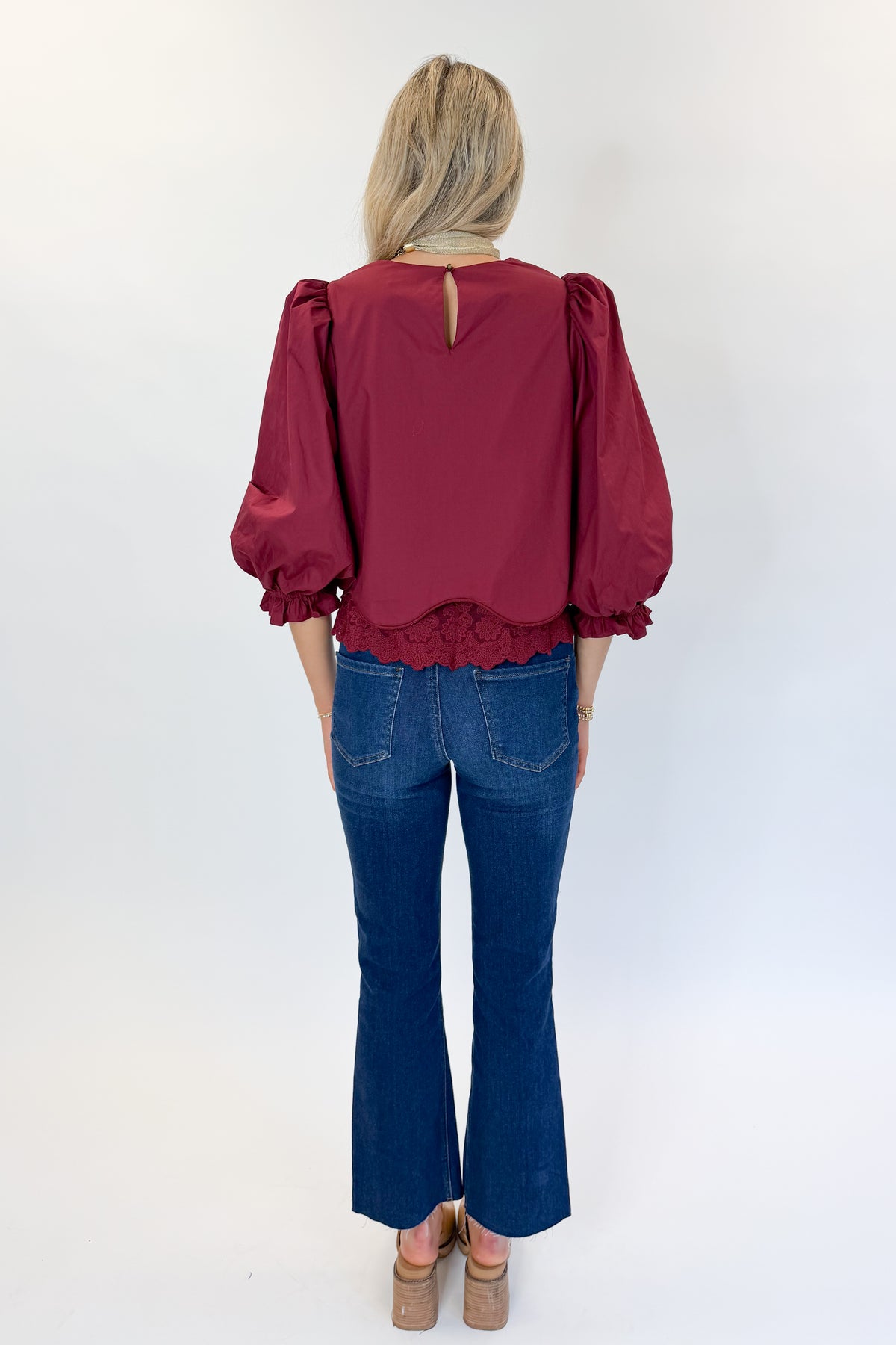 Back view of woman wearing Swagger Boutique’s Wine Lace Trim Top by Entro with jeans against white studio background.