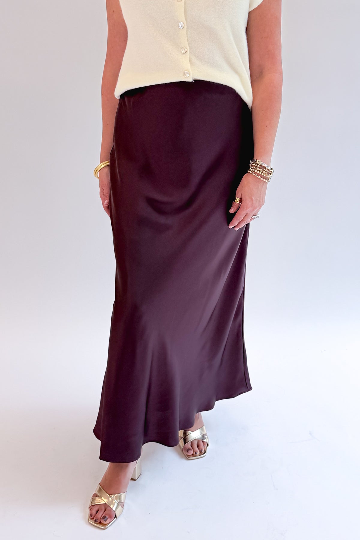 Front detail view of woman wearing Swagger Boutique’s Wine Satin Maxi Skirt with sweater against white studio background.