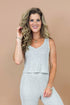 Woman wearing a light gray sleeveless top and pants against a beige background