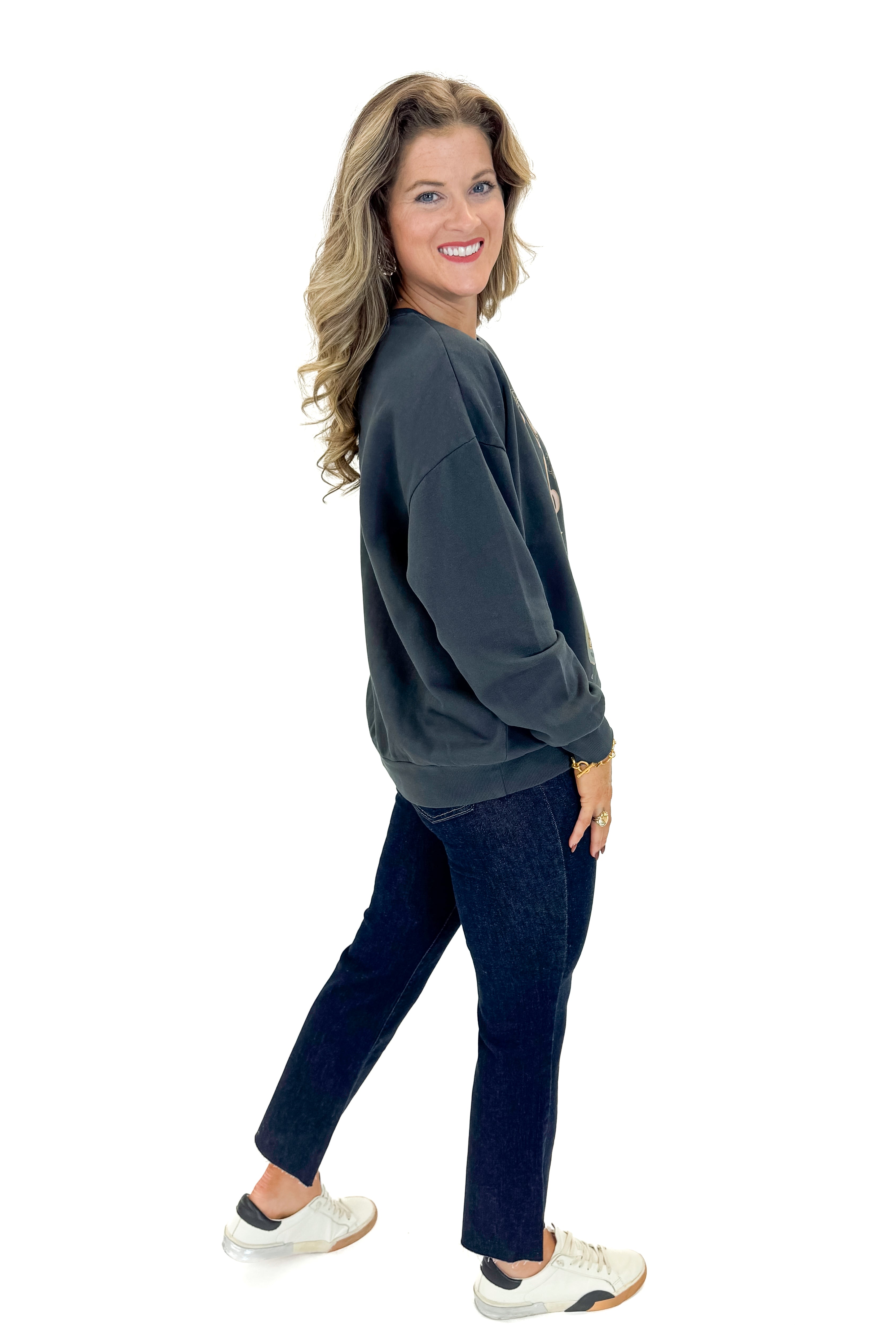 Side view of woman wearing Black Celebrate Sunday Sweatshirt with jeans against white studio background.