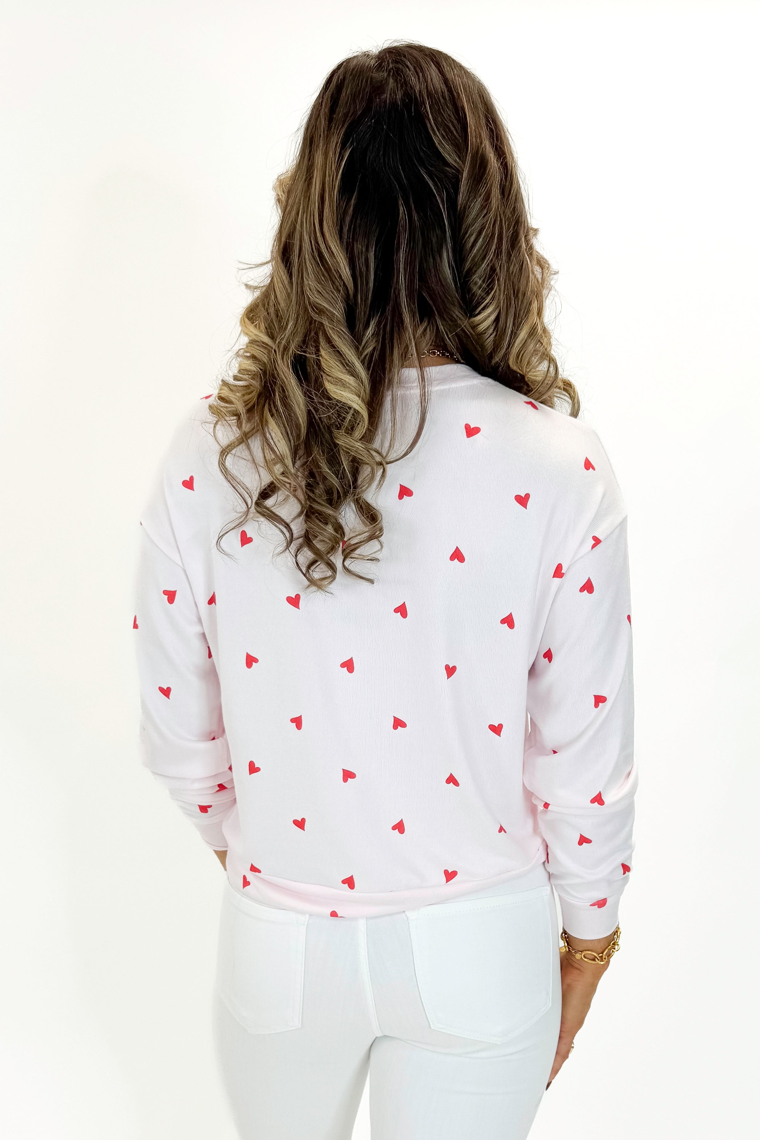 Back view of woman wearing Pink Marshmallow Mira Heart Top with jeans against white studio background.