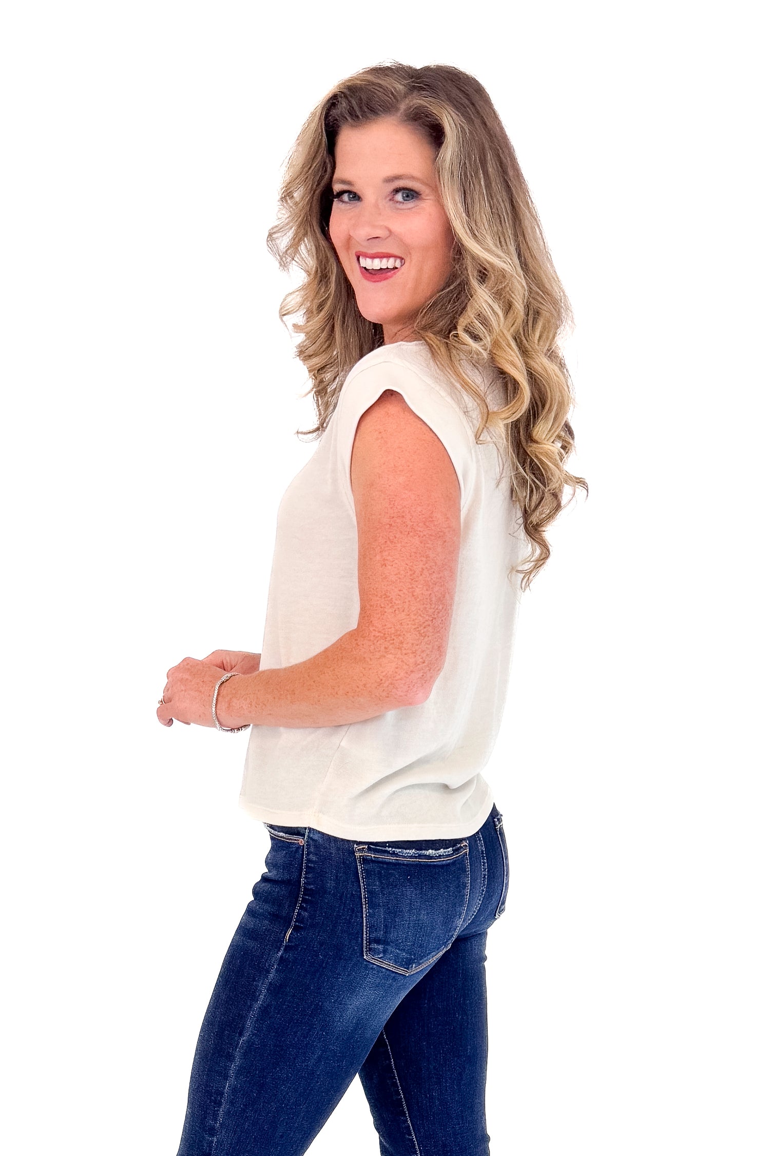 Woman wearing a white sleeveless top and blue jeans on a white background