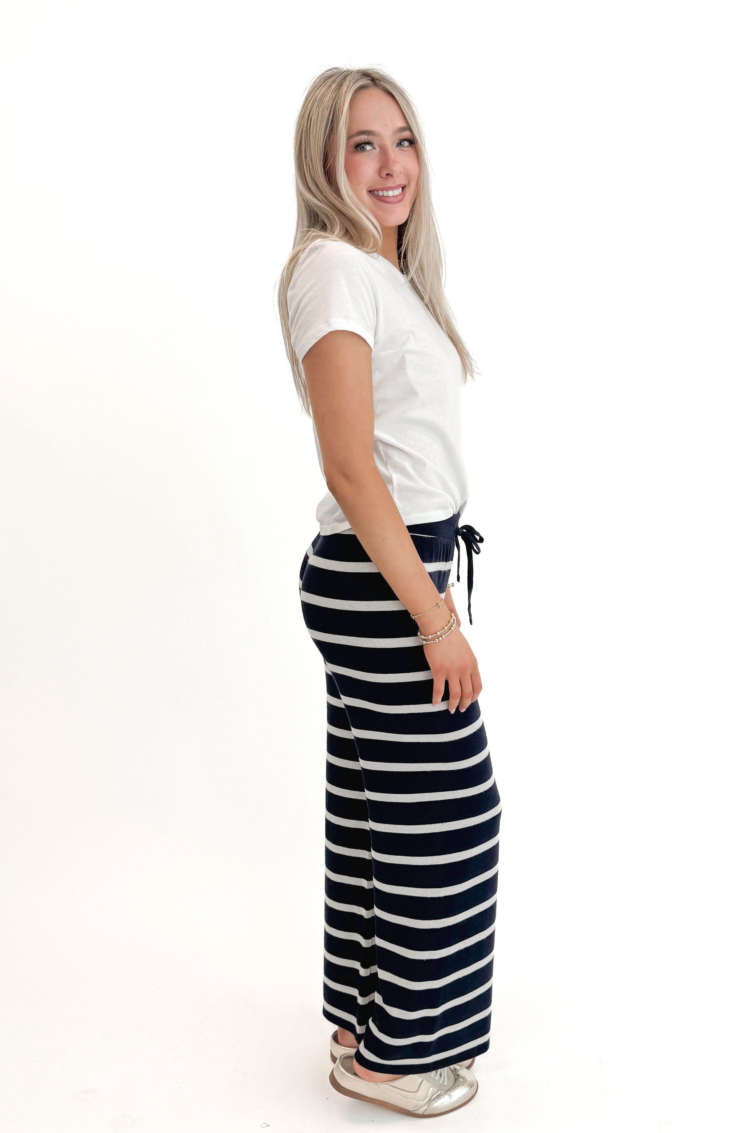 Side view of woman wearing White Junie Tee Shirt by Z Supply with pants against white studio background.