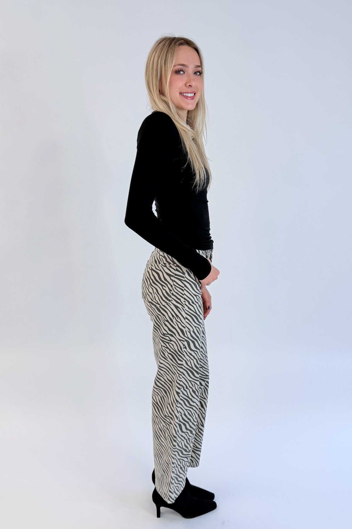Side view of woman wearing Swagger Boutique’s top with Zebra Straight Leg Jeans by Just Black Denim against white studio background.