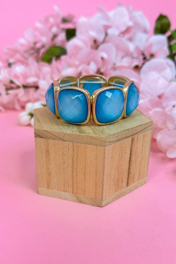 Blue bracelet with gold accents on a wooden block against a pink floral background