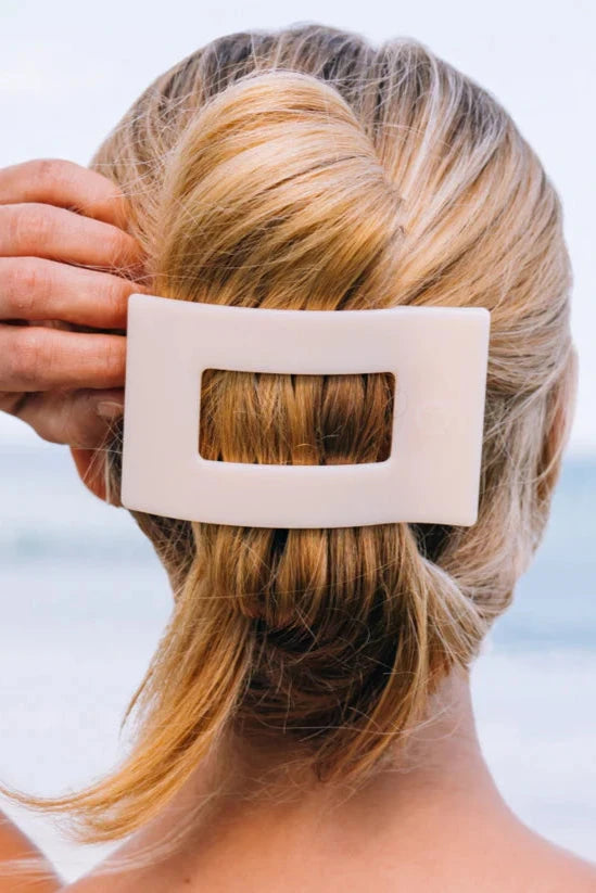 Person with blonde hair wearing a beige rectangular hair clip against a blurred natural background