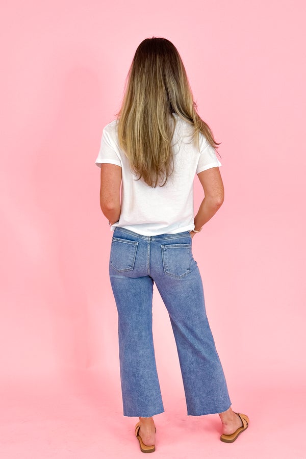 Person wearing a white t-shirt and blue jeans against a pink background