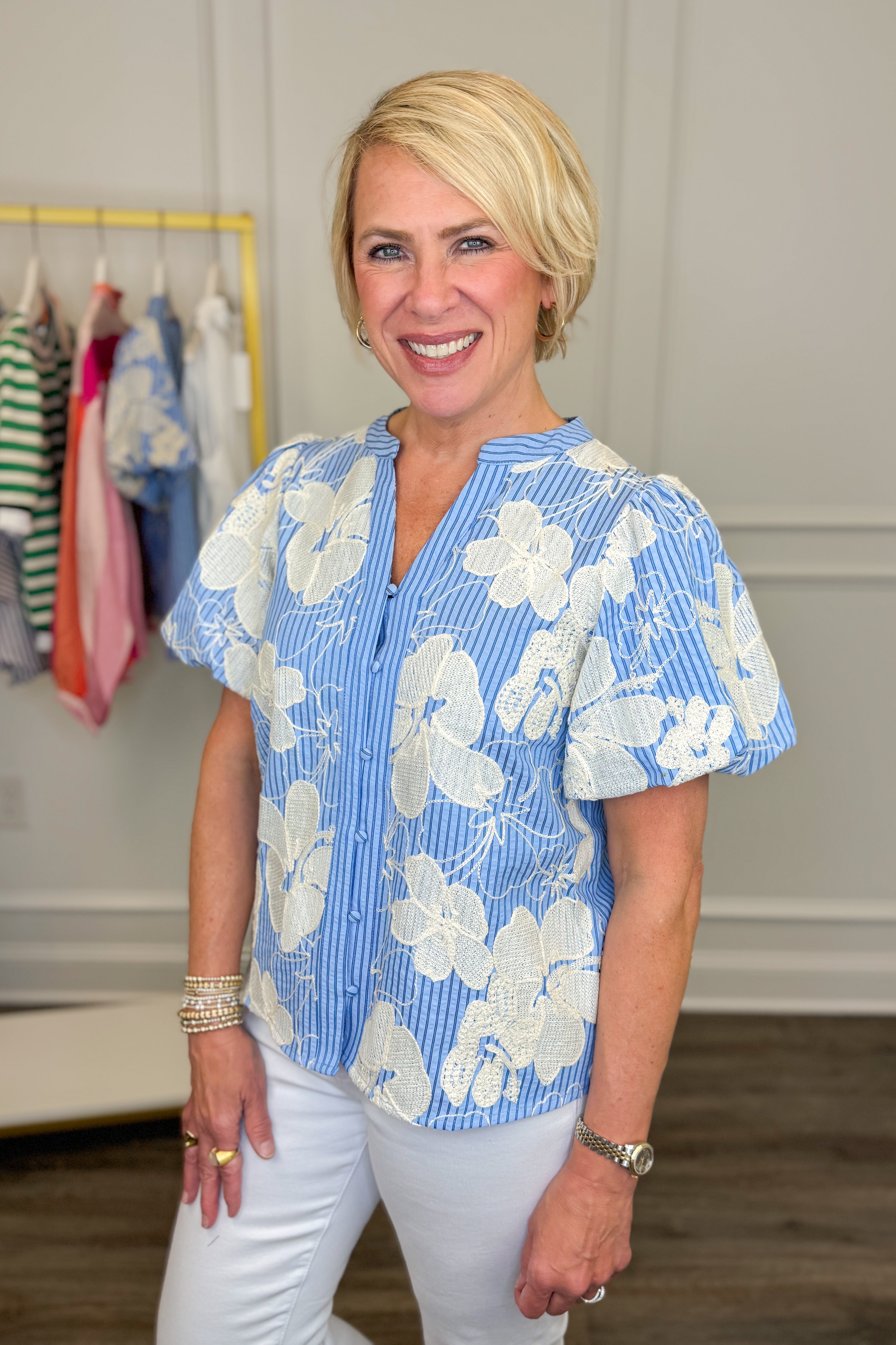 Woman wearing a blue floral blouse in a room with clothes on a rack.