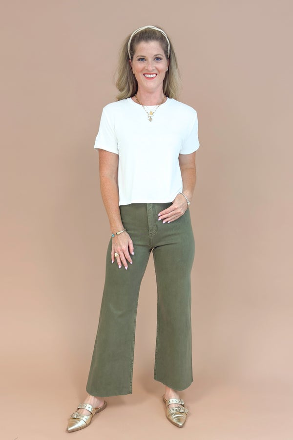 Woman wearing a white t-shirt and green pants on a beige background