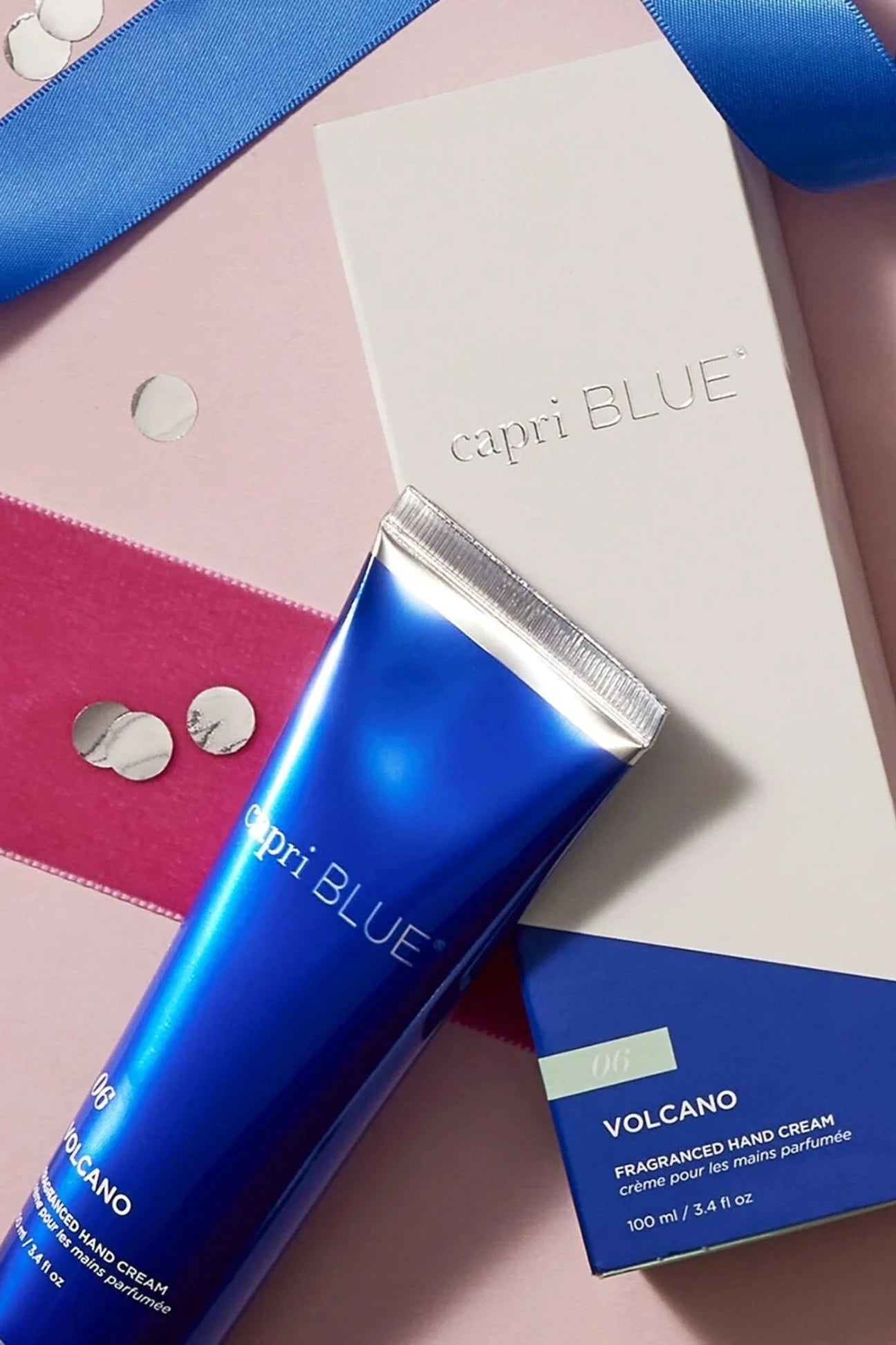 Capri Blue Volcano fragranced hand cream on a pink background with decorative ribbons and buttons.