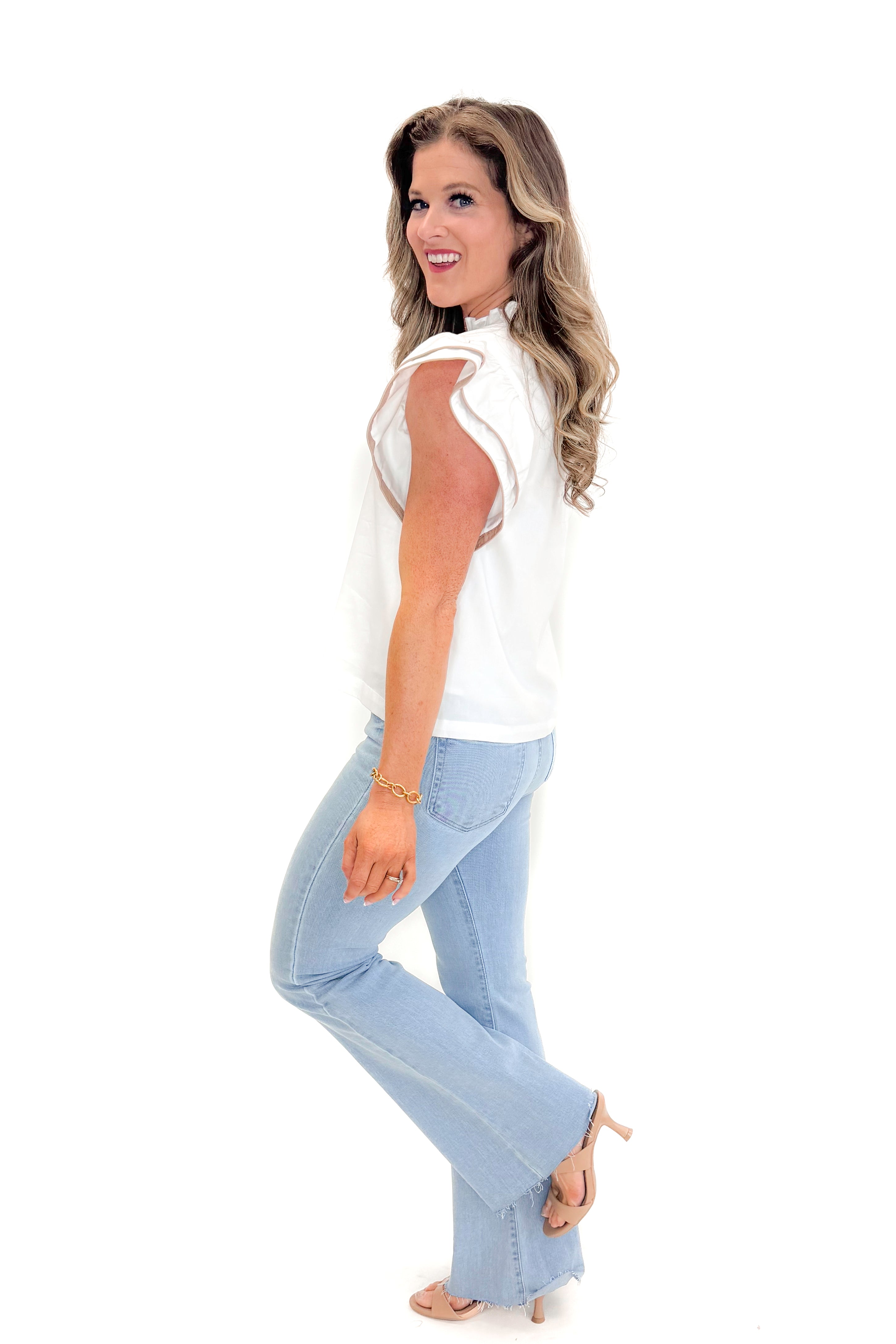 Side view of woman wearing White With Taupe Piping Detail Top with jeans against white studio background.
