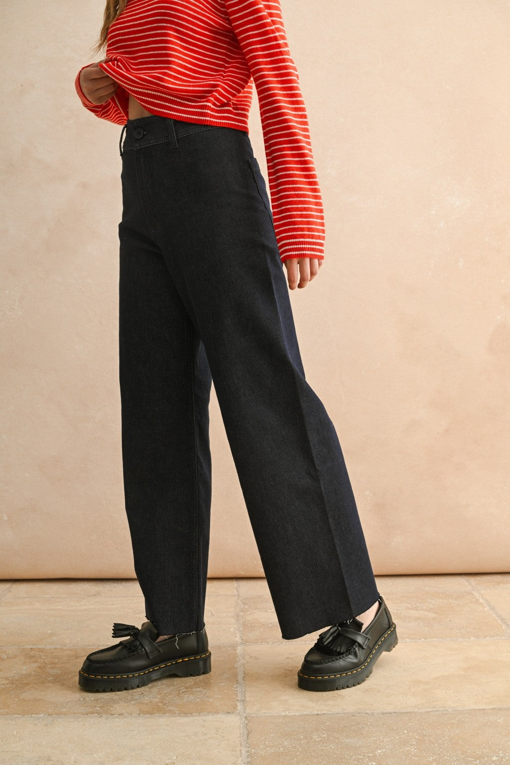 Side view of woman in a studio wearing Dark Indigo Wide Leg Jeans and print top with a tan background.