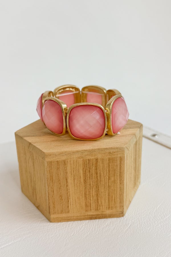 Pink bracelet with gold accents on a wooden block against a white background