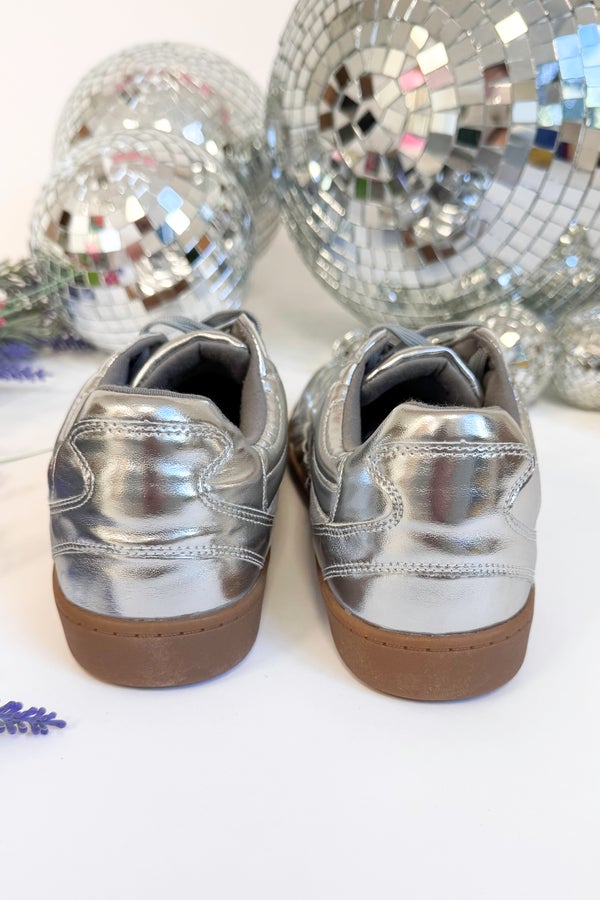 Silver metallic shoes with brown soles on a white background with disco balls.
