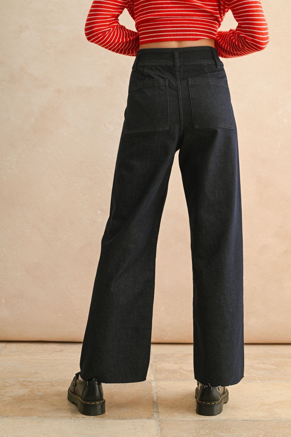 Back view of woman in a studio wearing Dark Indigo Wide Leg Jeans and print top with a tan background.